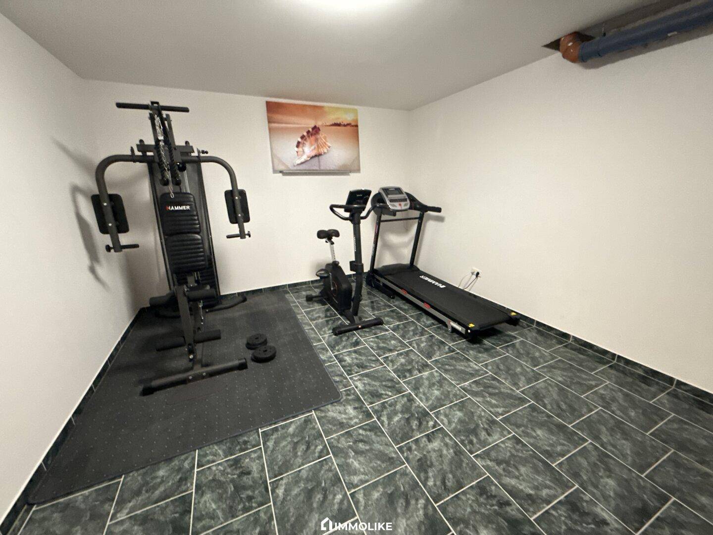Fitnessraum im Keller mit verschiedenen Trainingsgeräten und Fliesenboden.