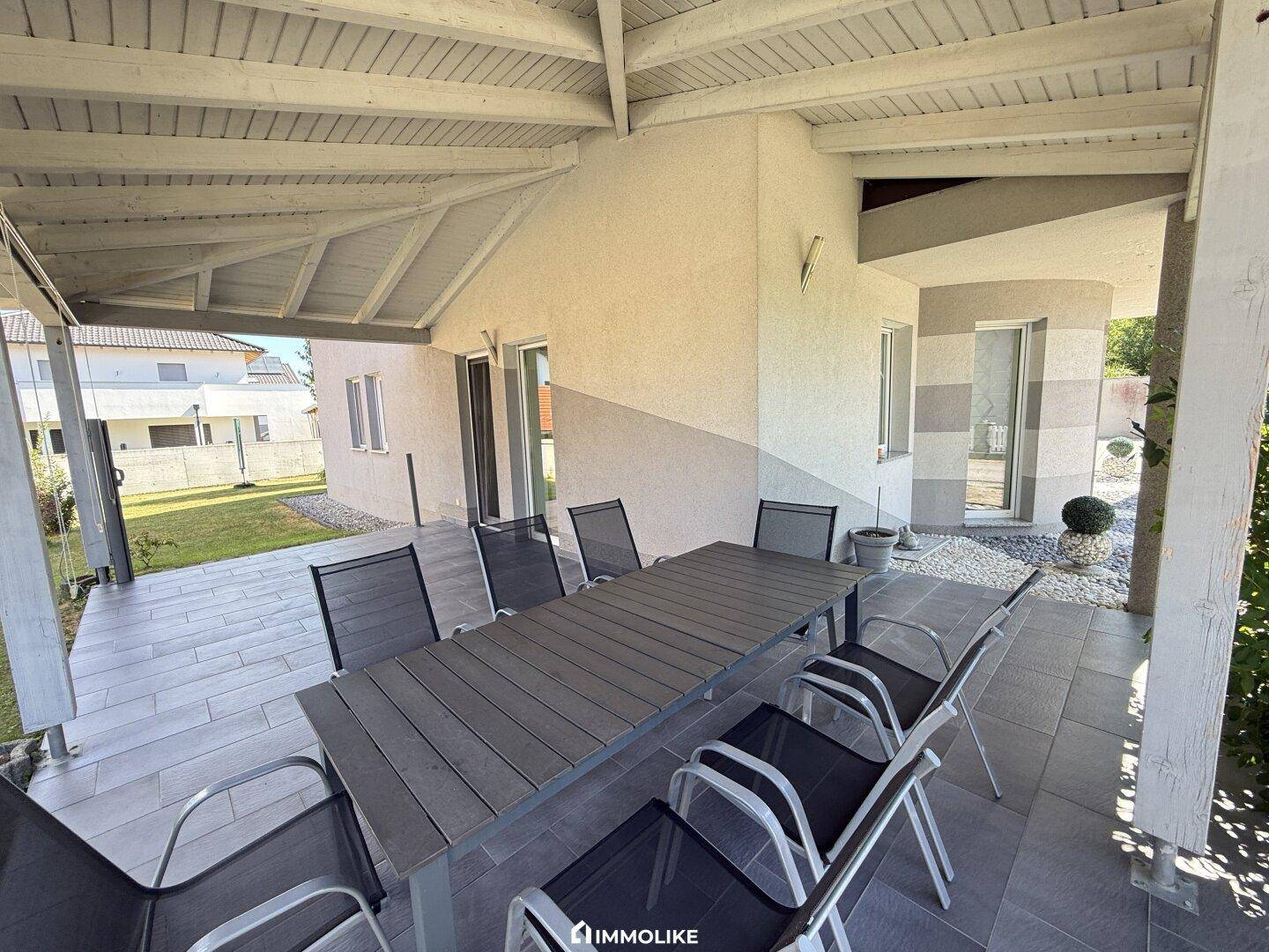Überdachte Terrasse mit großem Esstisch und Stühlen, ideal für Mahlzeiten im Freien.