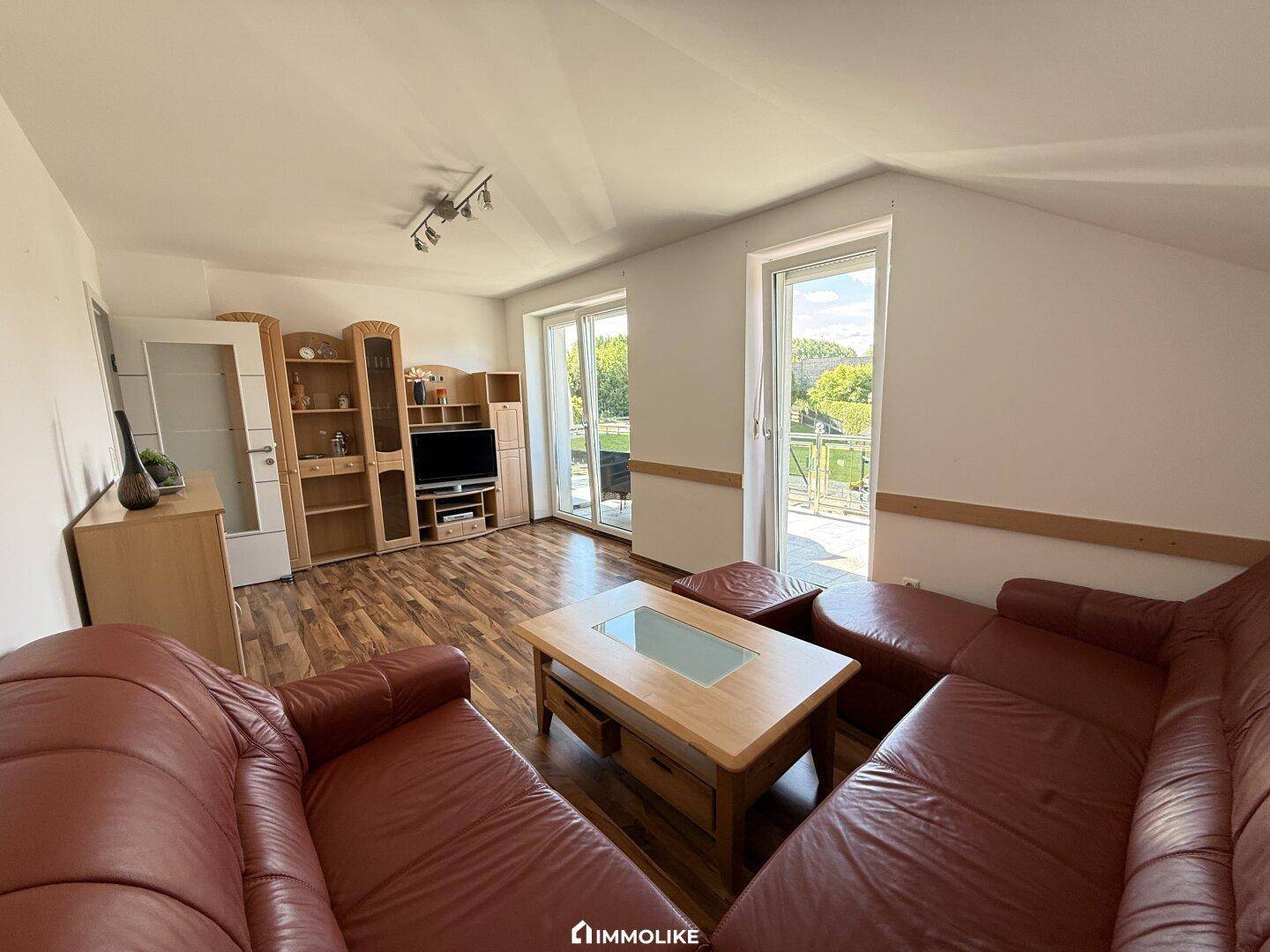 Gemütliches Wohnzimmer im Dachgeschoss mit Holzfußboden und Zugang zu einem Balkon.