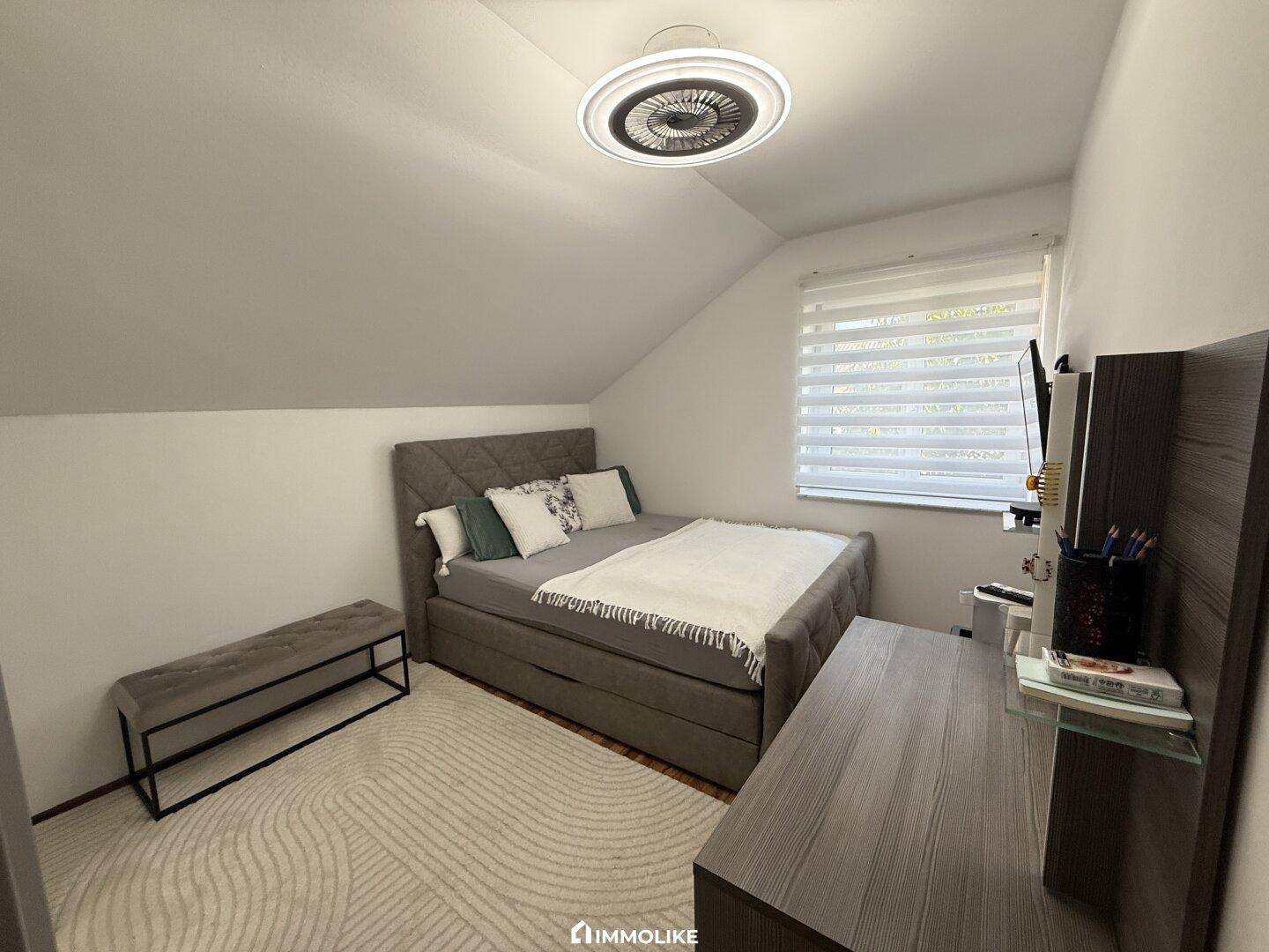 Helles Schlafzimmer im Dachgeschoss mit modernem Bett, Teppichboden und Dachschräge.