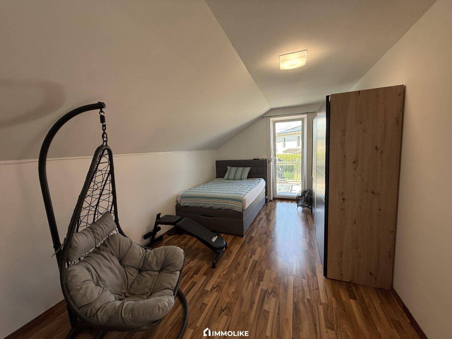 Schlafzimmer mit Holzfußboden, Einzelbett und einem Hängesessel, ideal als Gästezimmer.