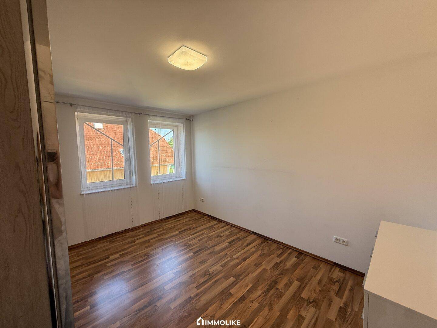 Helles Schlafzimmer mit Holzfußboden und zwei Fenstern, bietet viel Tageslicht.