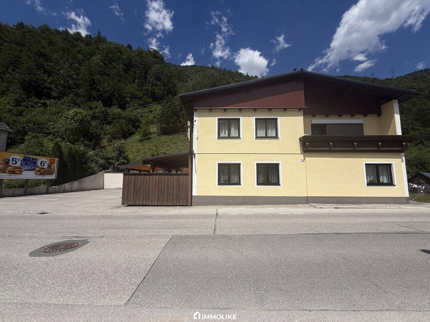 Rückansicht des Gebäudes mit gelber Fassade, dunklen Fenstern und einem Balkon im oberen Stockwerk.