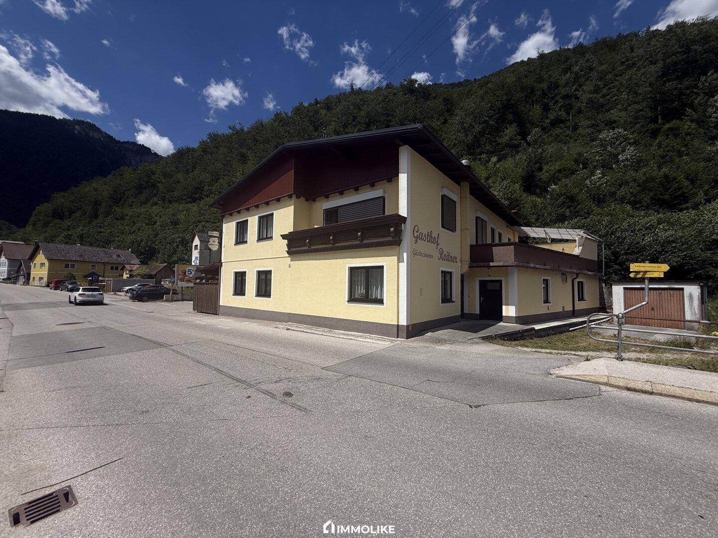 Gasthausgebäude an einer Straße gelegen, mit gelber Fassade und Blick auf die umliegende Berglandschaft.