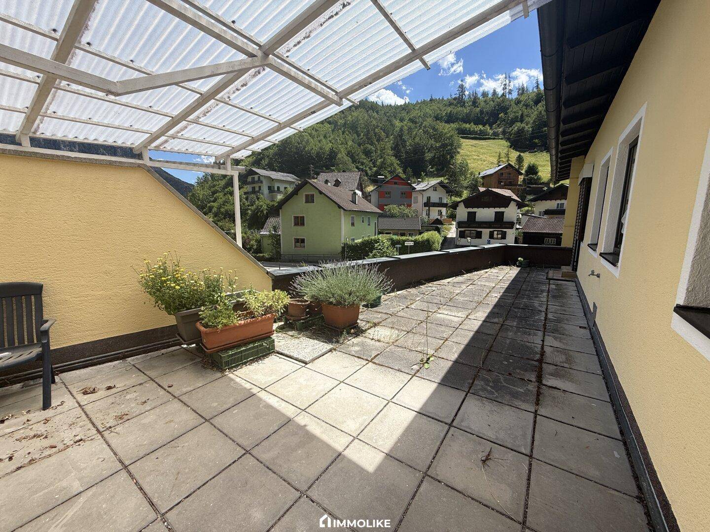 Überdachte Terrasse mit Pflanzen und Blick auf die umliegende Berglandschaft und Häuser.