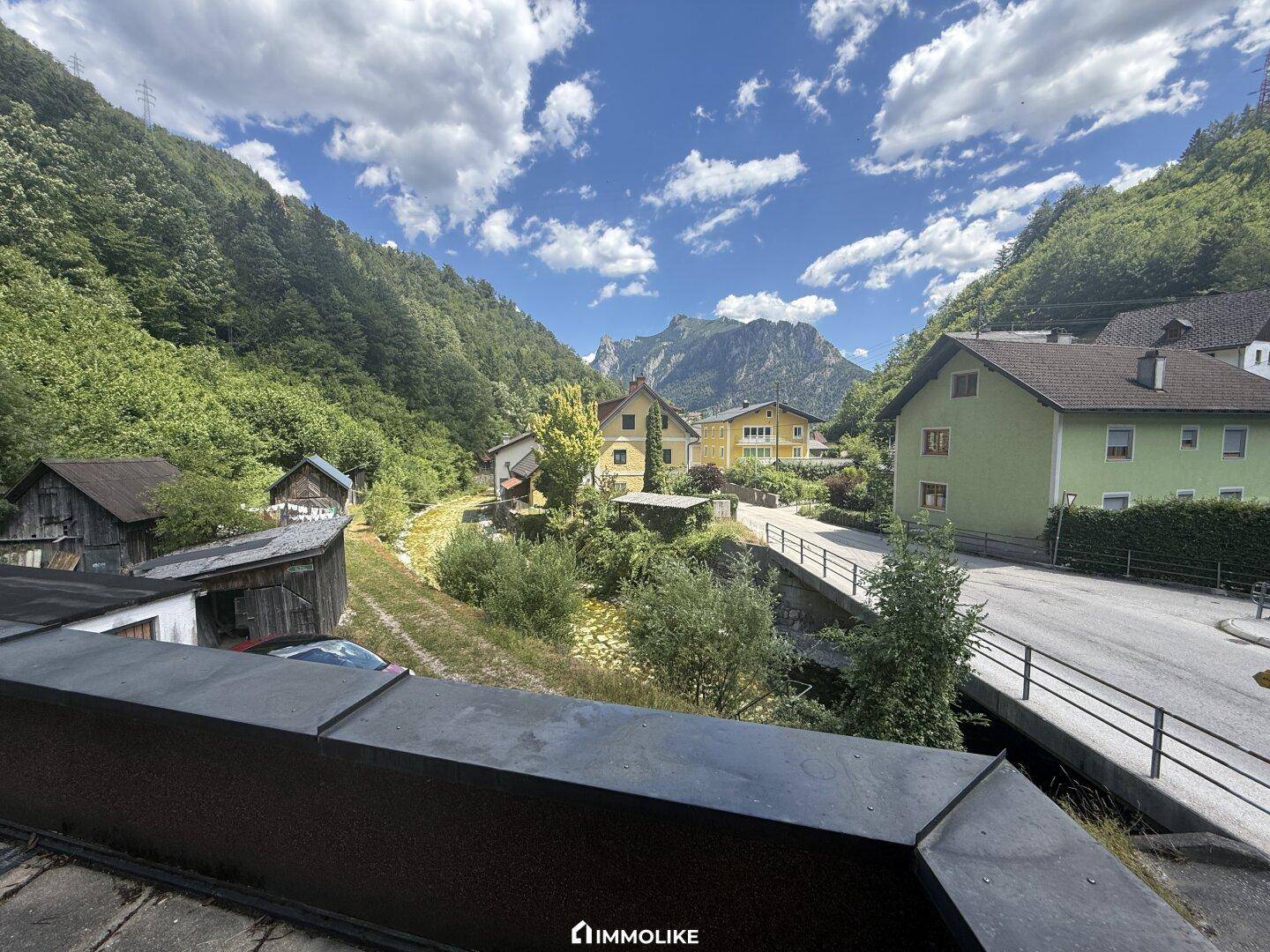 Malerischer Ausblick auf eine grüne Berglandschaft mit kleinen Häusern und einem Fluss.