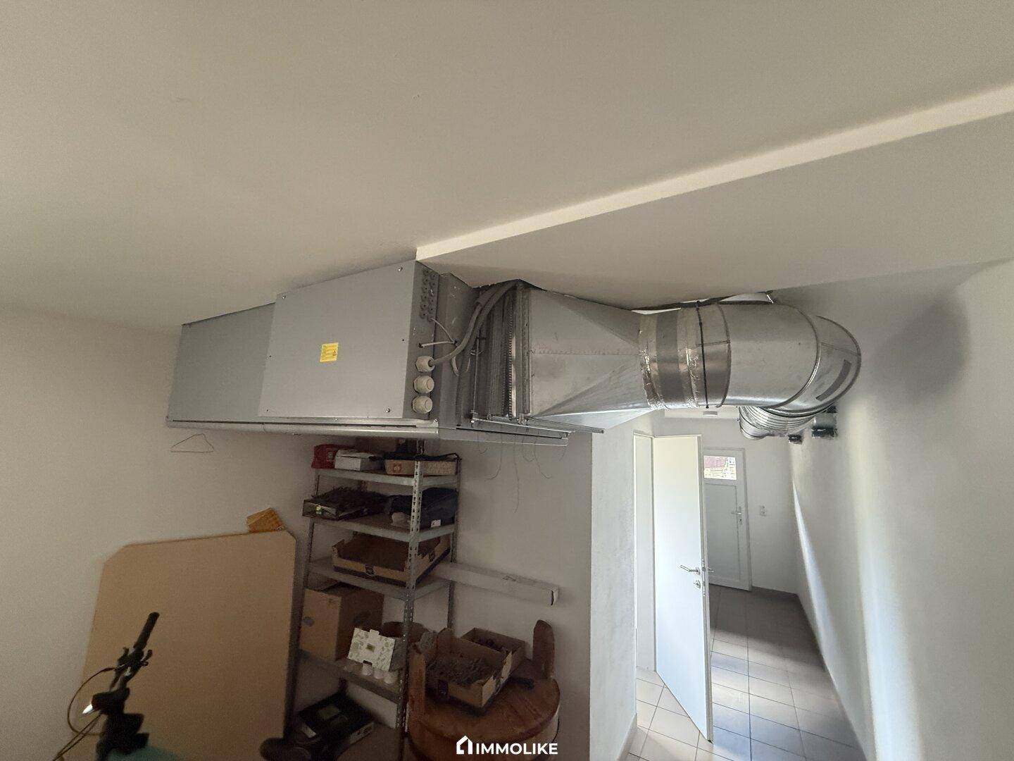 Technikraum mit sichtbaren Lüftungsrohren und Regalen für Lagerzwecke.