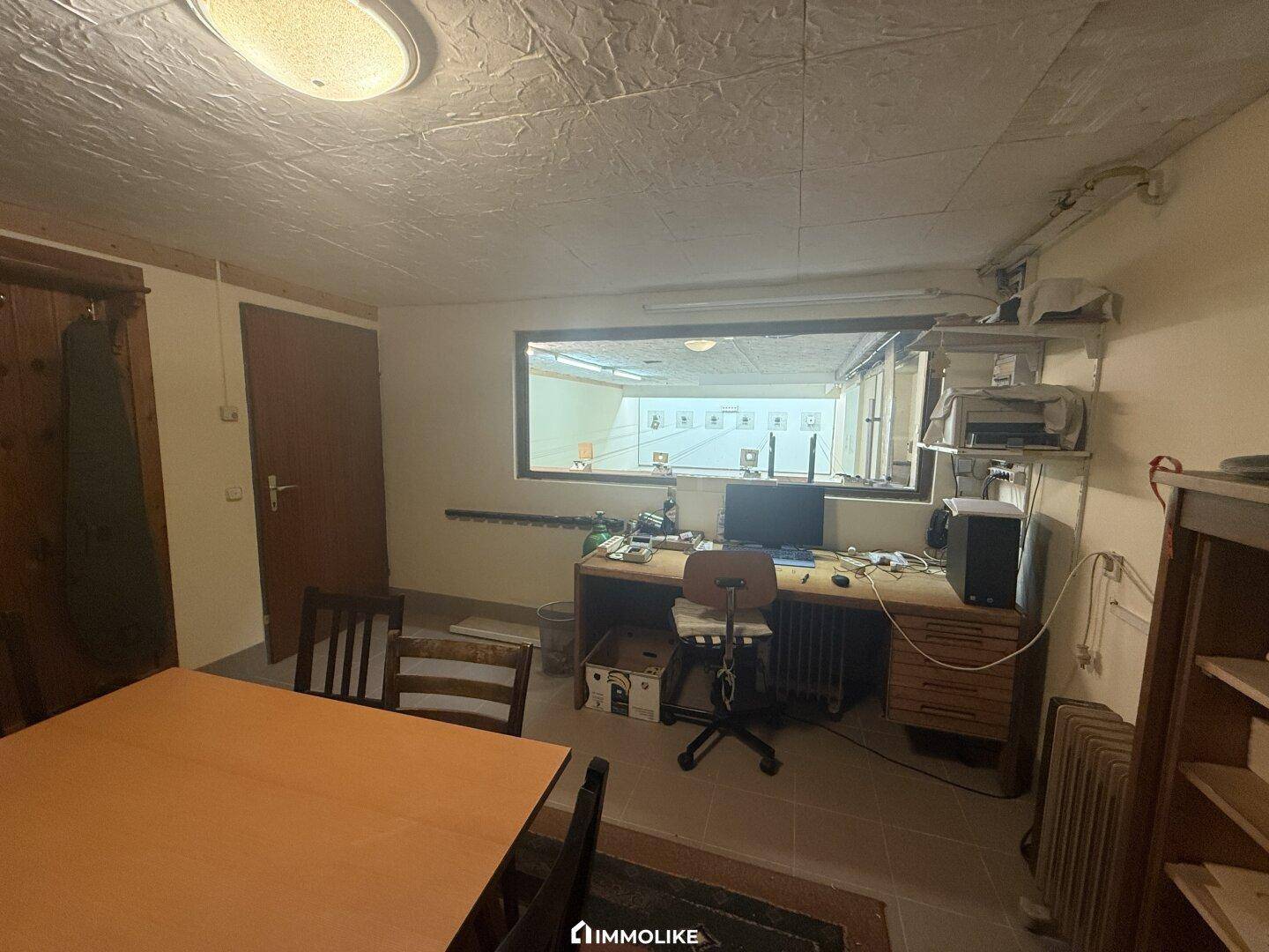 Kontrollraum für den Schießstand mit Schreibtisch, Monitor und Blick auf die Anlage.
