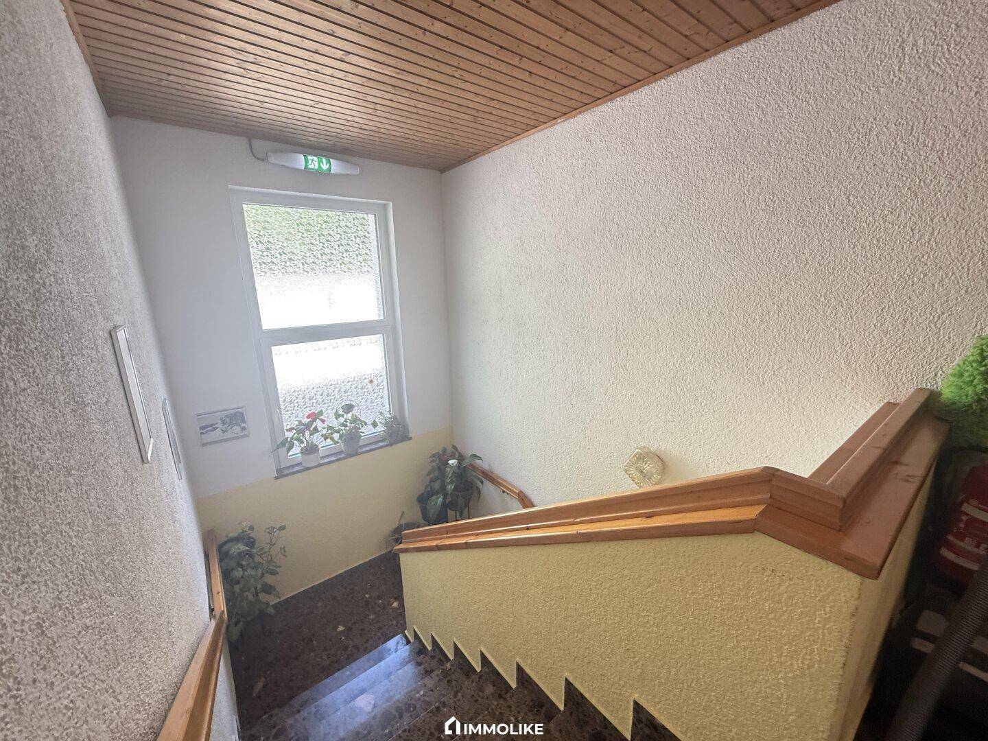 Treppenhaus mit Holzgeländer, strukturierten Wänden und einem Fenster für natürliches Licht.