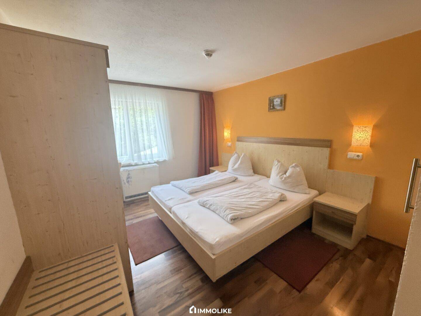 Gemütliches Schlafzimmer mit Doppelbett, Holzmöbeln und orangefarbener Akzentwand.