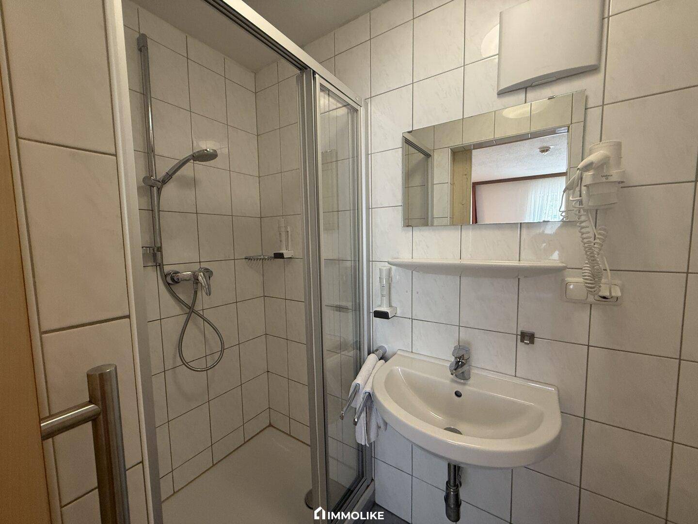 Kleines Badezimmer mit Duschkabine, Waschbecken und weißen Fliesen.