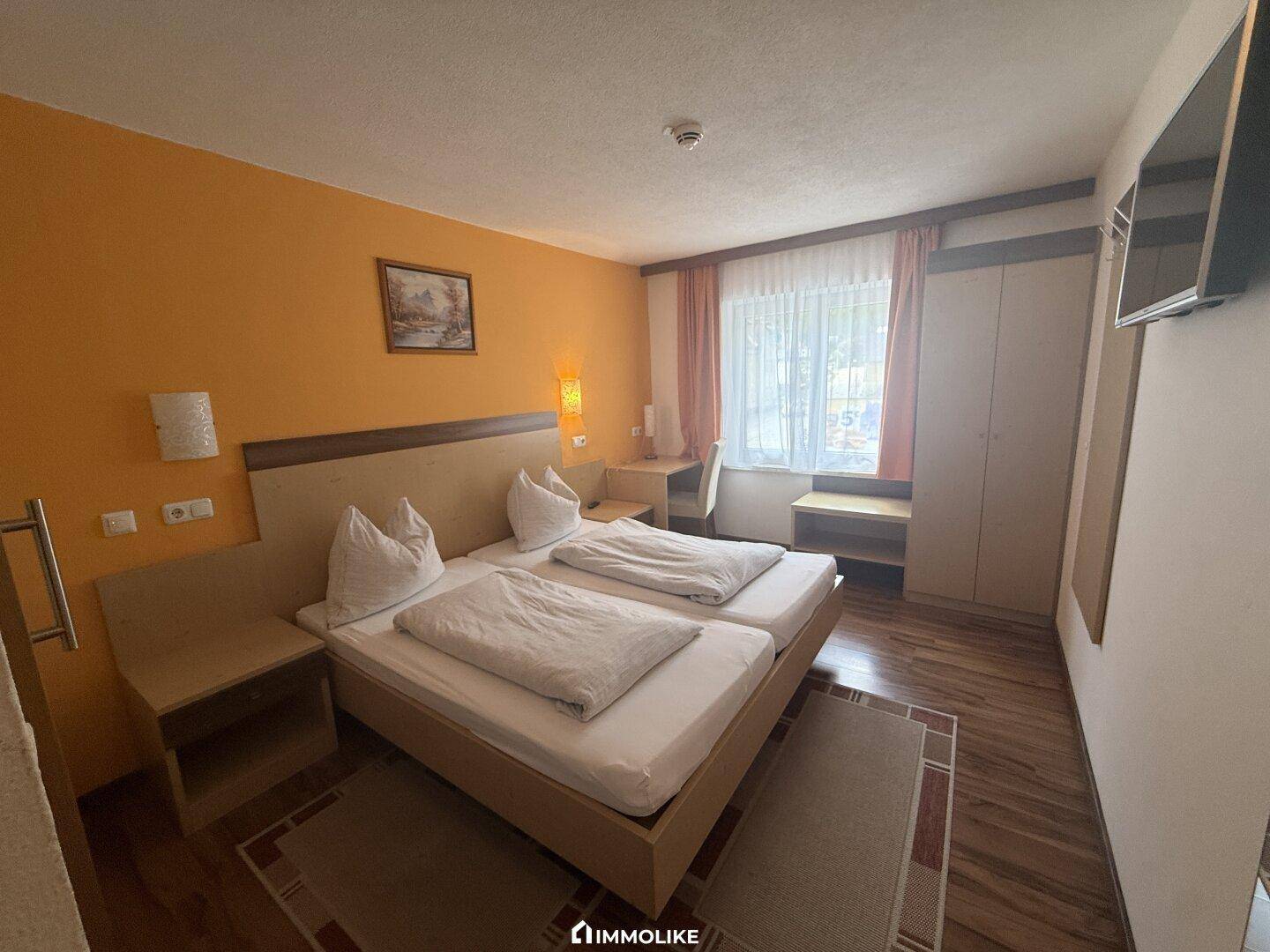 Schlafzimmer mit zwei Einzelbetten, Schreibtisch und Fernseher, in warmen Farbtönen gehalten.