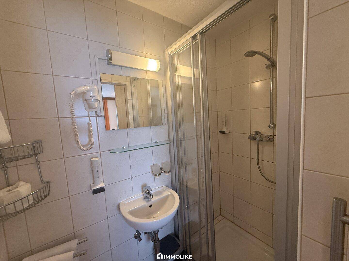 Funktionales Badezimmer mit Duschkabine, Waschbecken und hellen Fliesen.
