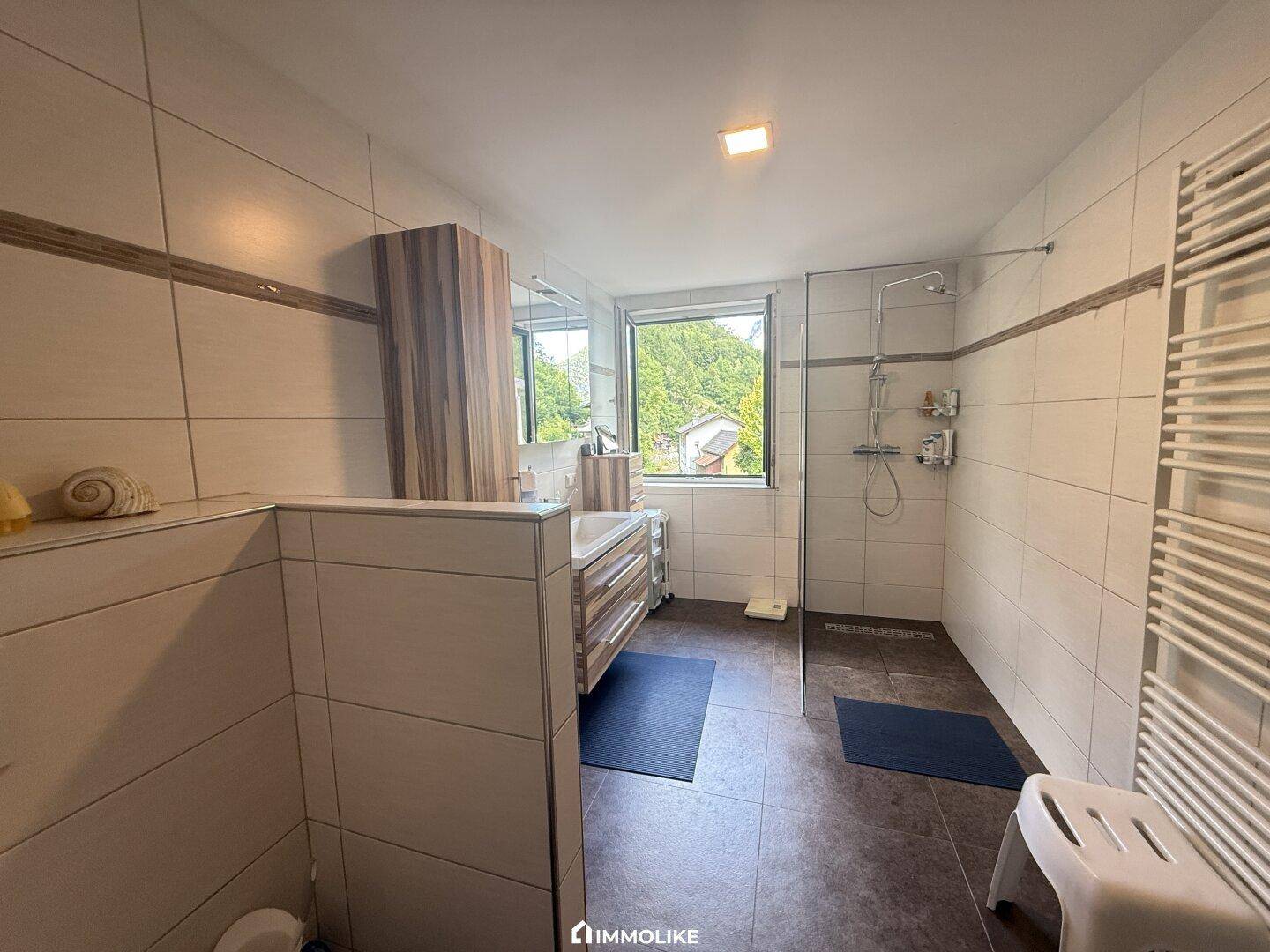 Modernes Badezimmer mit großer Dusche, Doppelwaschbecken und Fenster mit Grünblick.