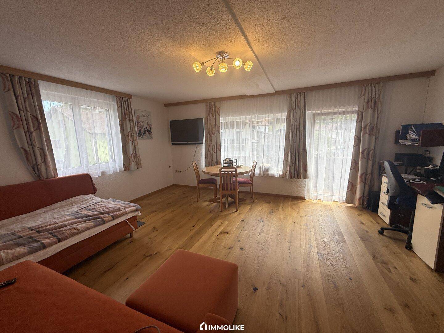 Geräumiges Wohnzimmer mit Holzboden, Sofa und Esstisch, hell durch mehrere Fenster.