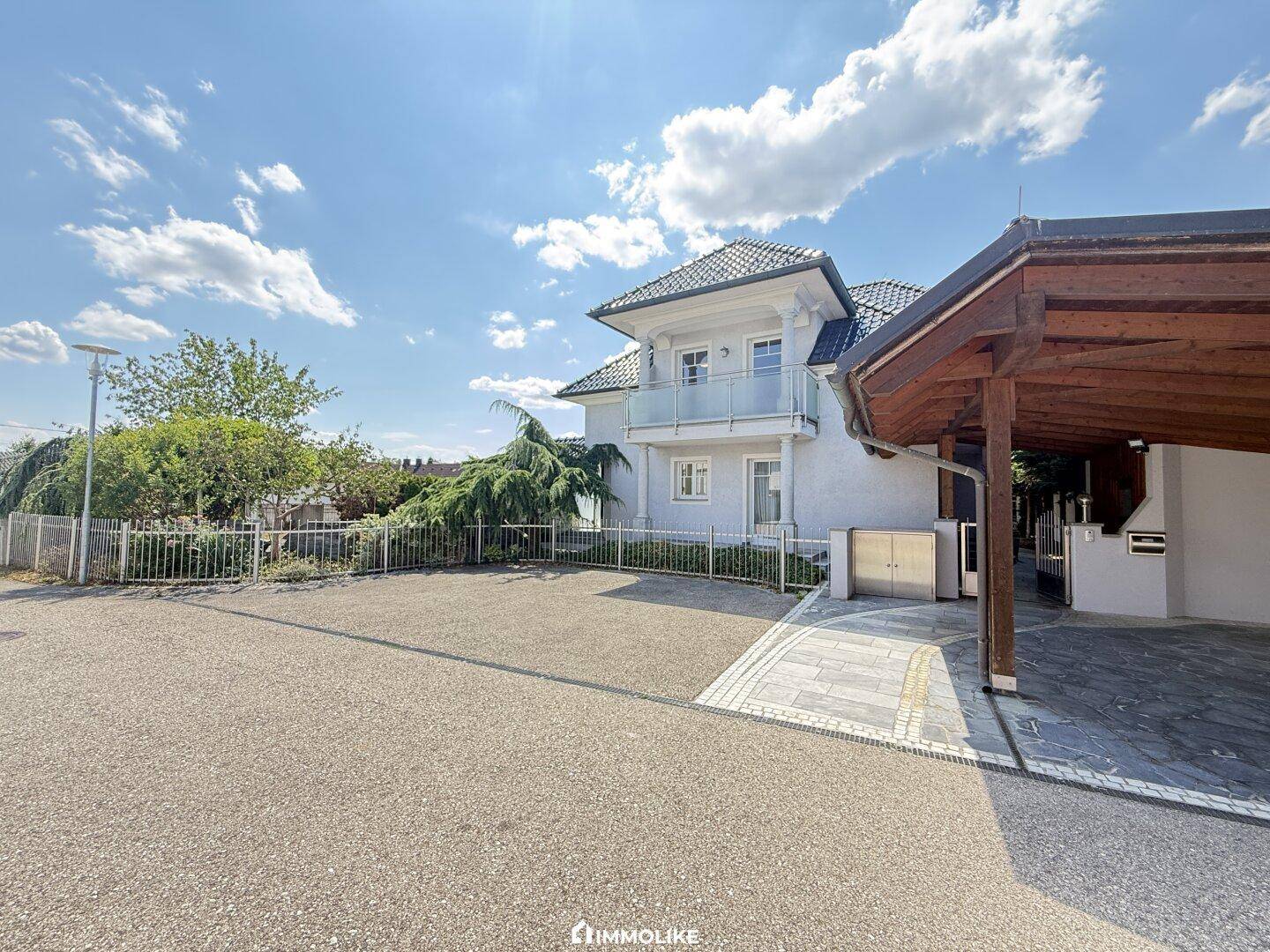 Vorderansicht des Hauses mit großem Vorplatz und einem überdachten Carport für Fahrzeuge.