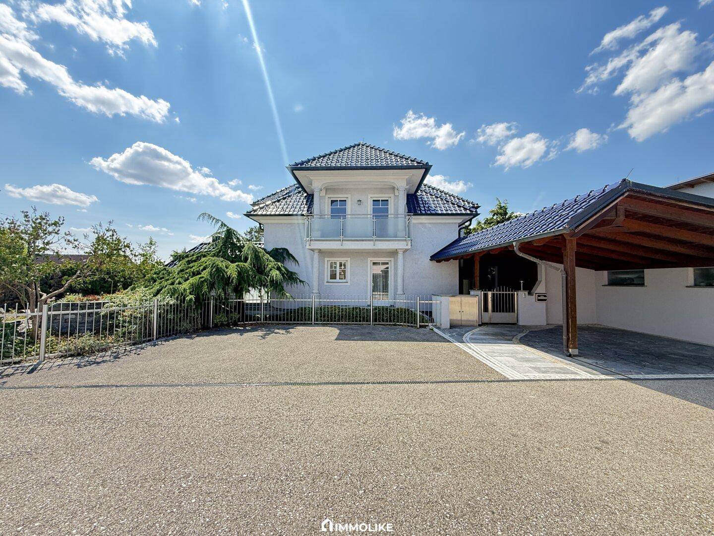 Ansicht des Hauses von der Einfahrt mit einem geräumigen Parkplatz und einem Carport.