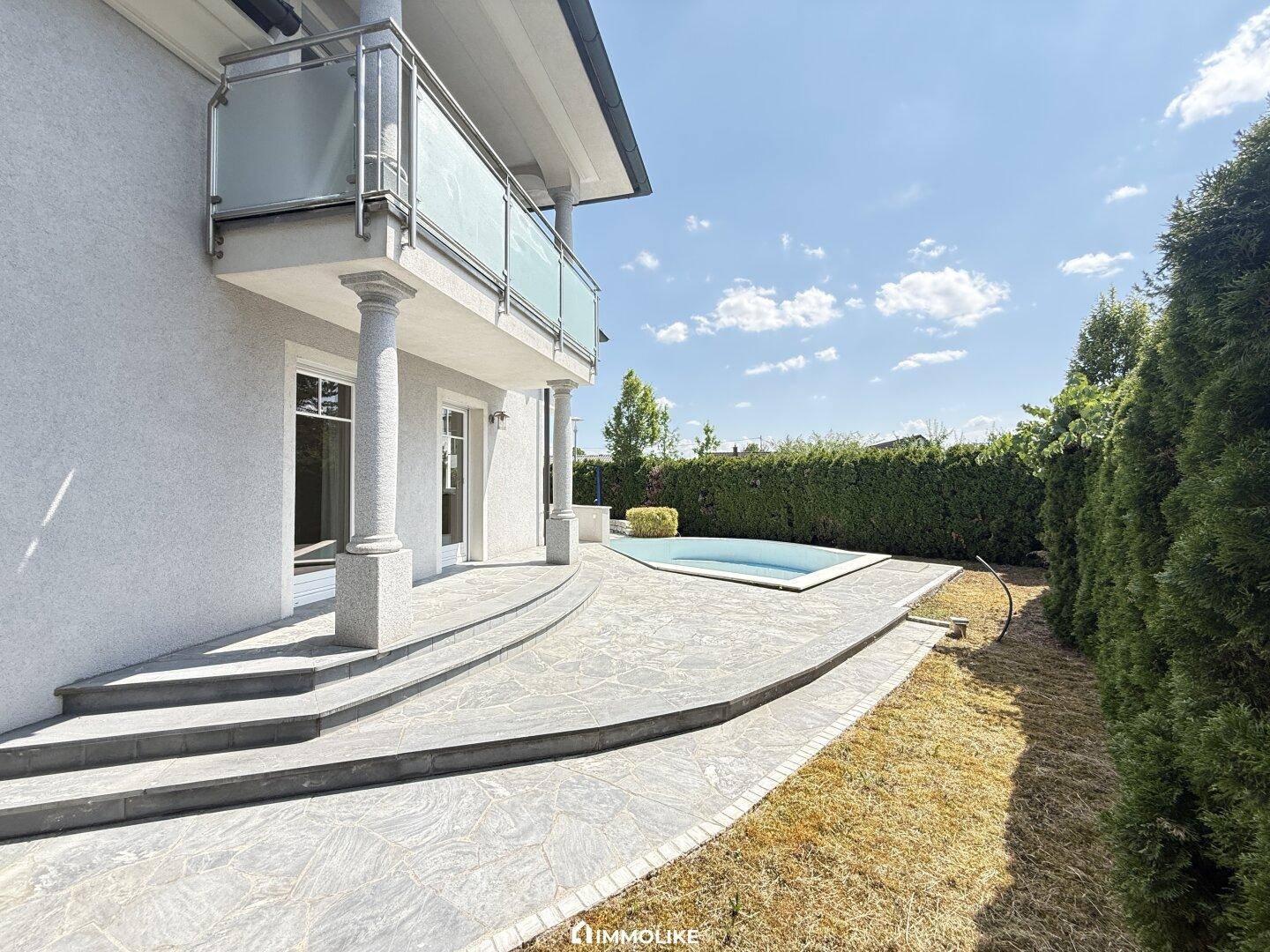 Seitliche Terrasse mit Zugang zum Poolbereich und Blick auf die gepflegte Hecke.