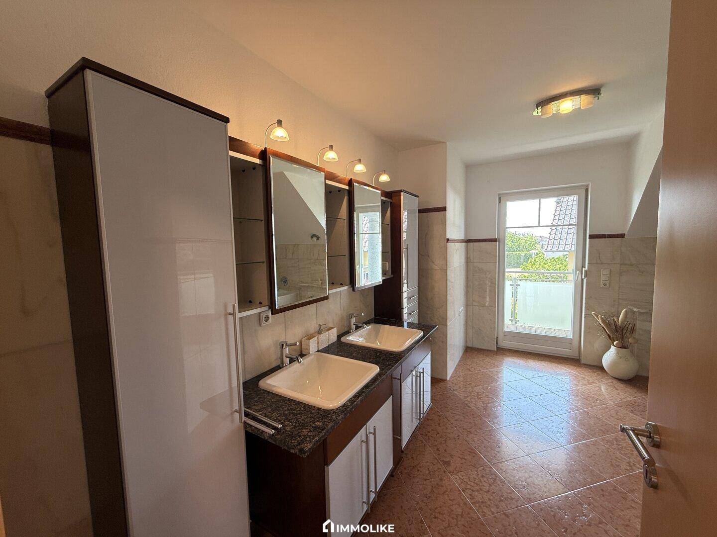 Modernes Badezimmer mit Doppelwaschbecken, Spiegelschränken und Zugang zu einem Balkon.