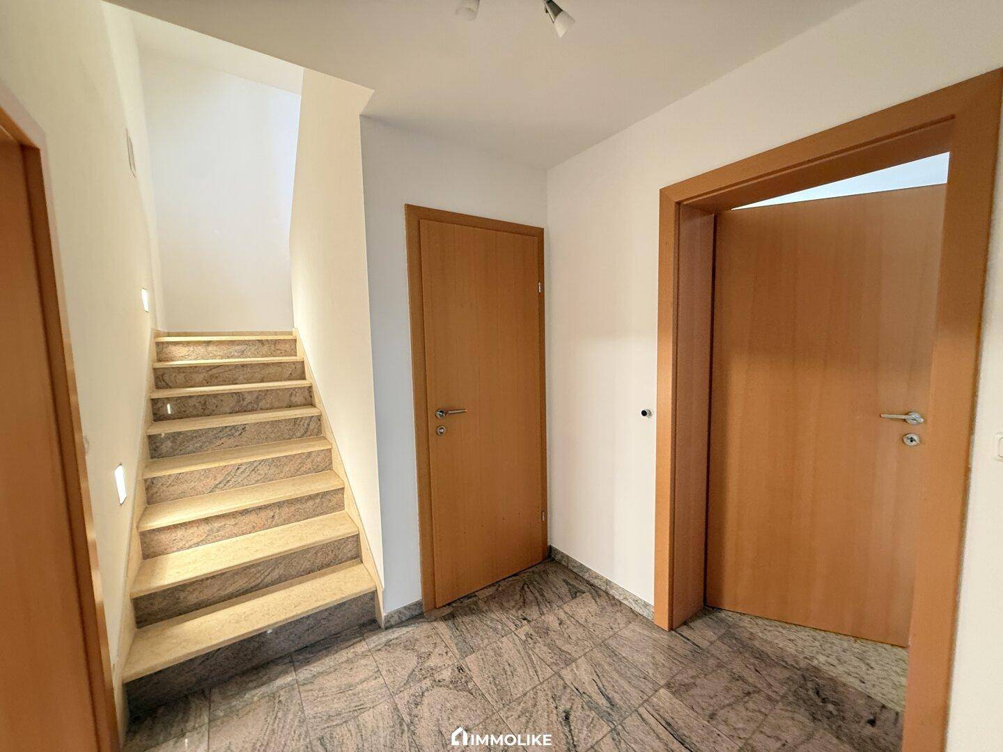 Heller Flur mit Steintreppe und Holztüren, die zu verschiedenen Räumen führen.