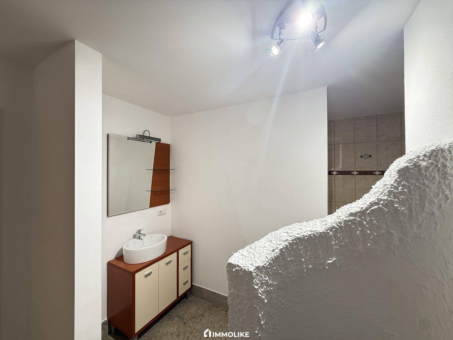 Badezimmer mit modernem Waschbecken, Spiegelschrank und einer Duschkabine im Hintergrund.
