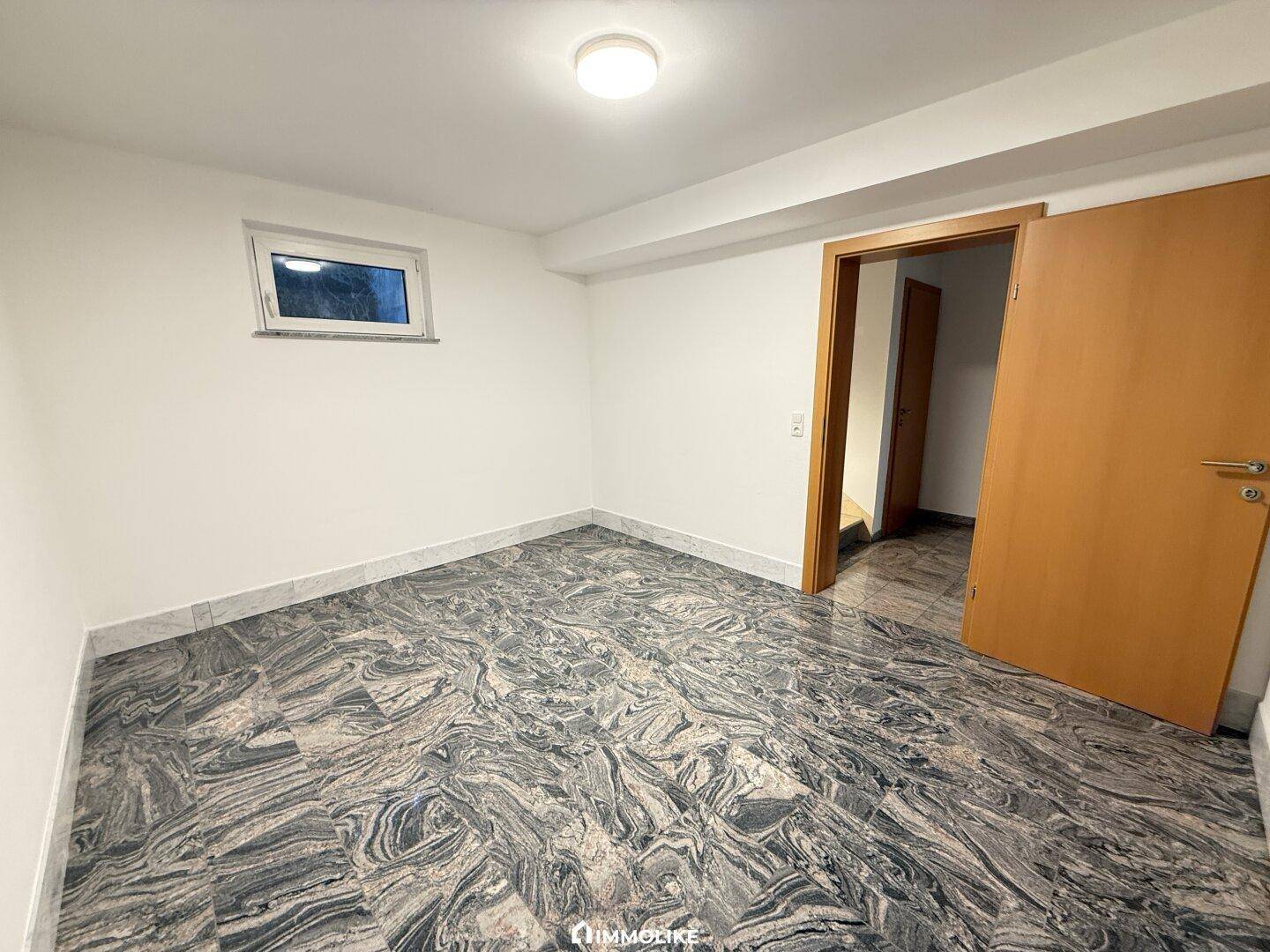 Unmöblierter Raum mit auffälligem Fliesenboden, kleinem Fenster und Holztür.