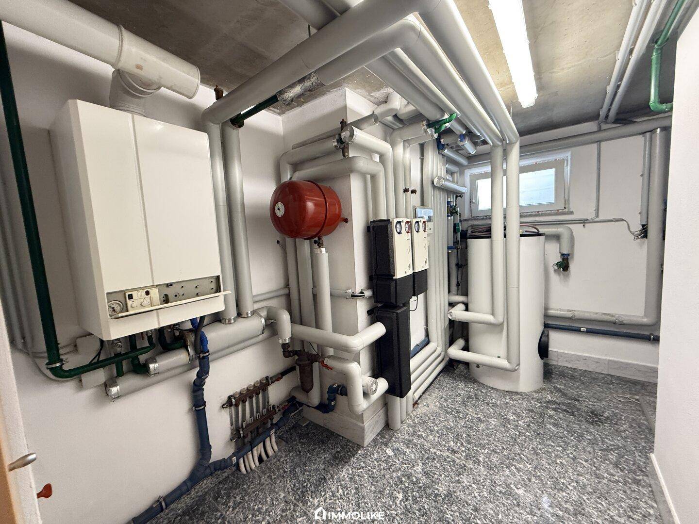 Technikraum mit Heizungsanlage, zahlreichen Rohren und kleinen Fenstern.