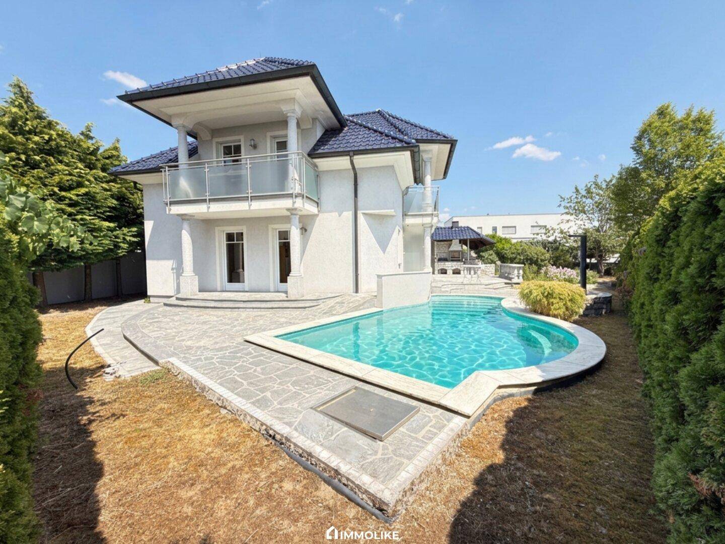 Hinterhof mit einem eleganten Swimmingpool und einer gepflasterten Terrasse, umgeben von Grünflächen.