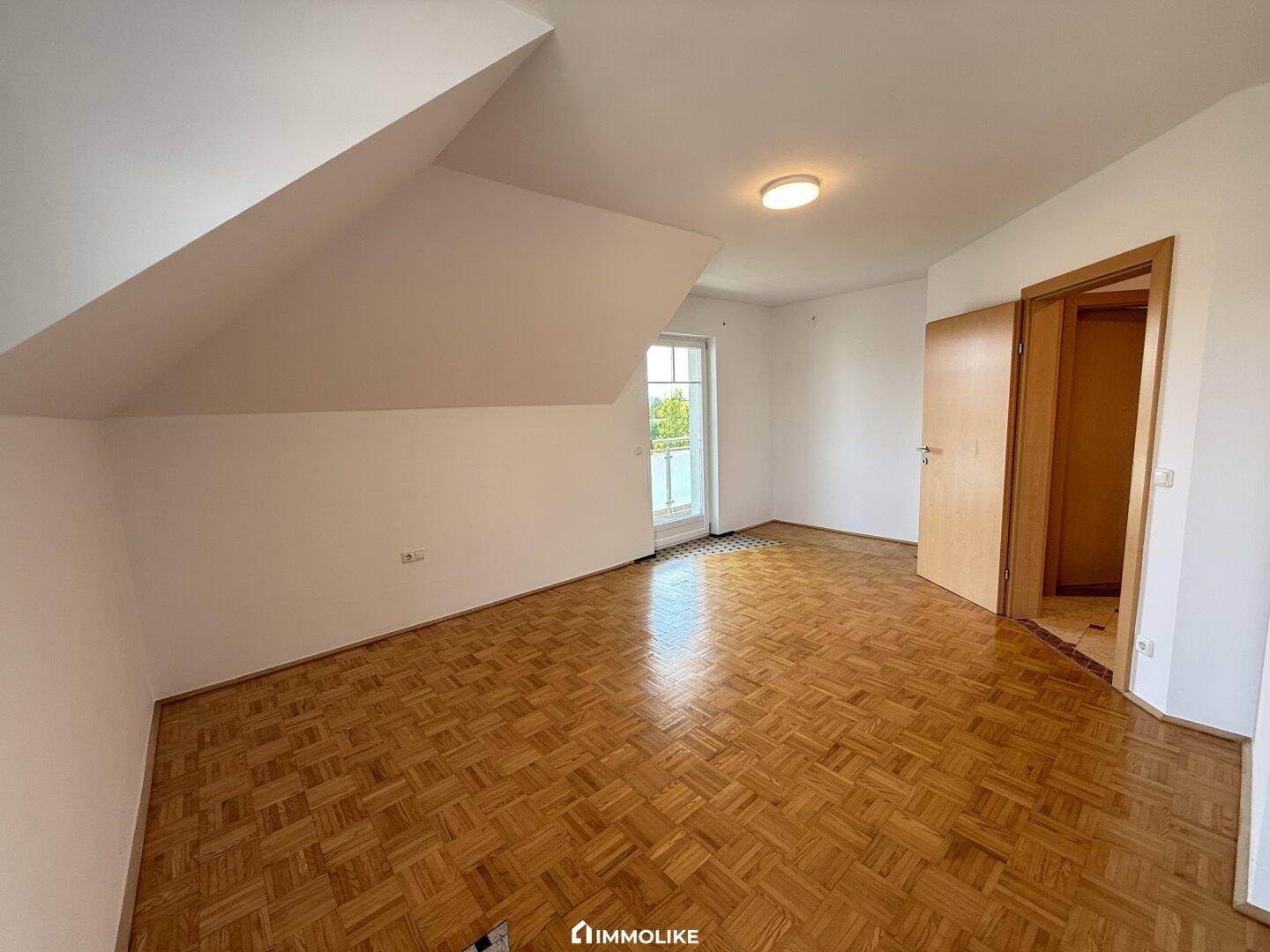 Helles Schlafzimmer mit Parkettboden und Zugang zu einem Balkon oder einer Terrasse.