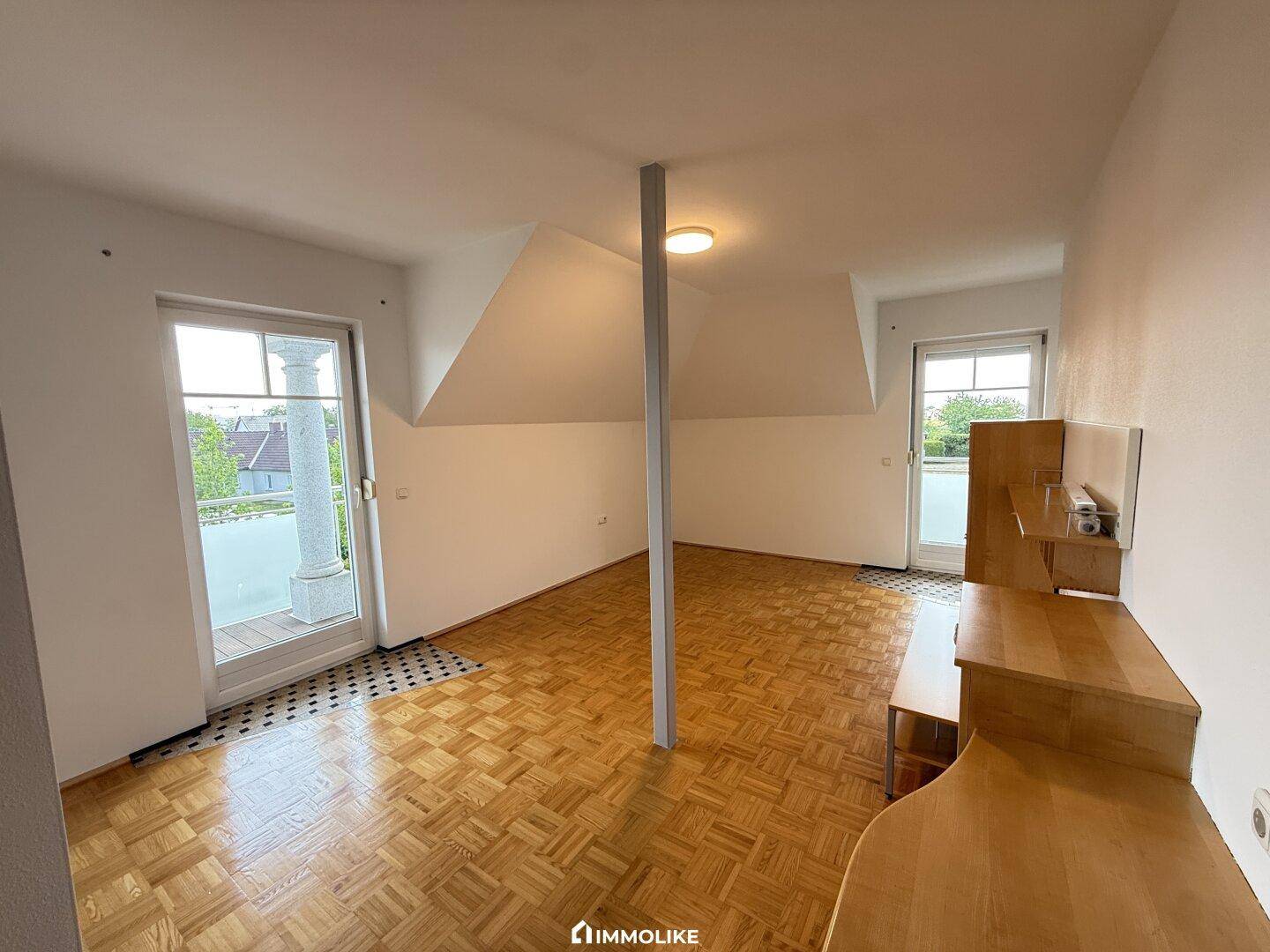 Geräumiges Schlafzimmer mit Parkettboden, Dachschrägen und zwei Fenstertüren zum Außenbereich.