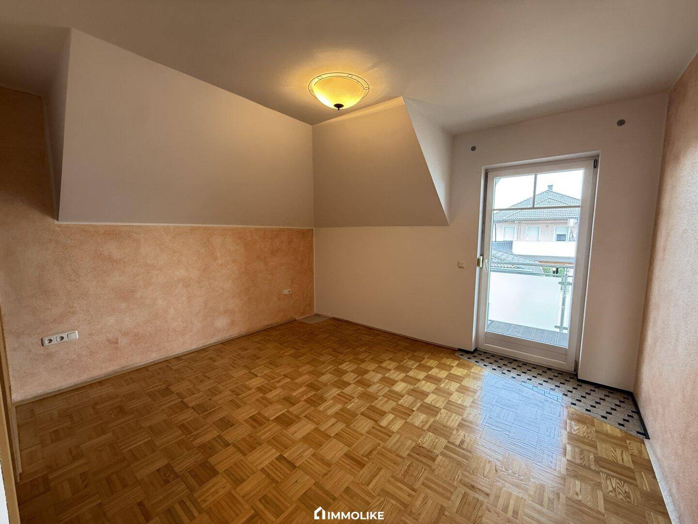 Gemütliches Schlafzimmer mit Parkettboden, Dachschräge und Zugang zu einem Balkon.