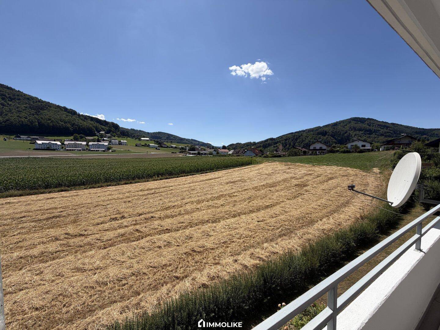 Weitläufiger Ausblick vom Balkon über goldene Felder und grüne Hügel unter blauem Himmel.