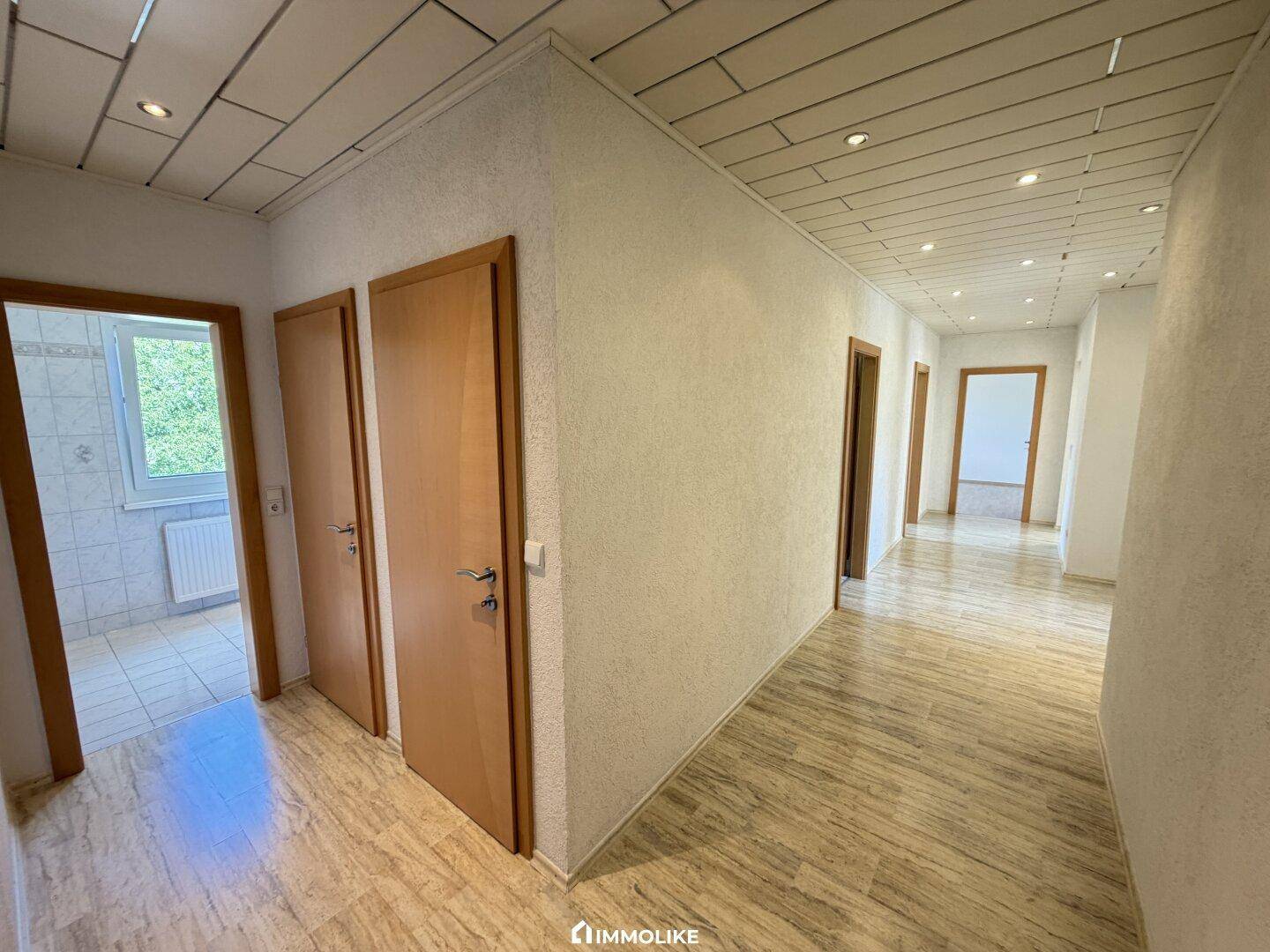 Heller Flur mit Holzoptik-Fliesenboden und mehreren Türen, beleuchtet durch Deckenspots.