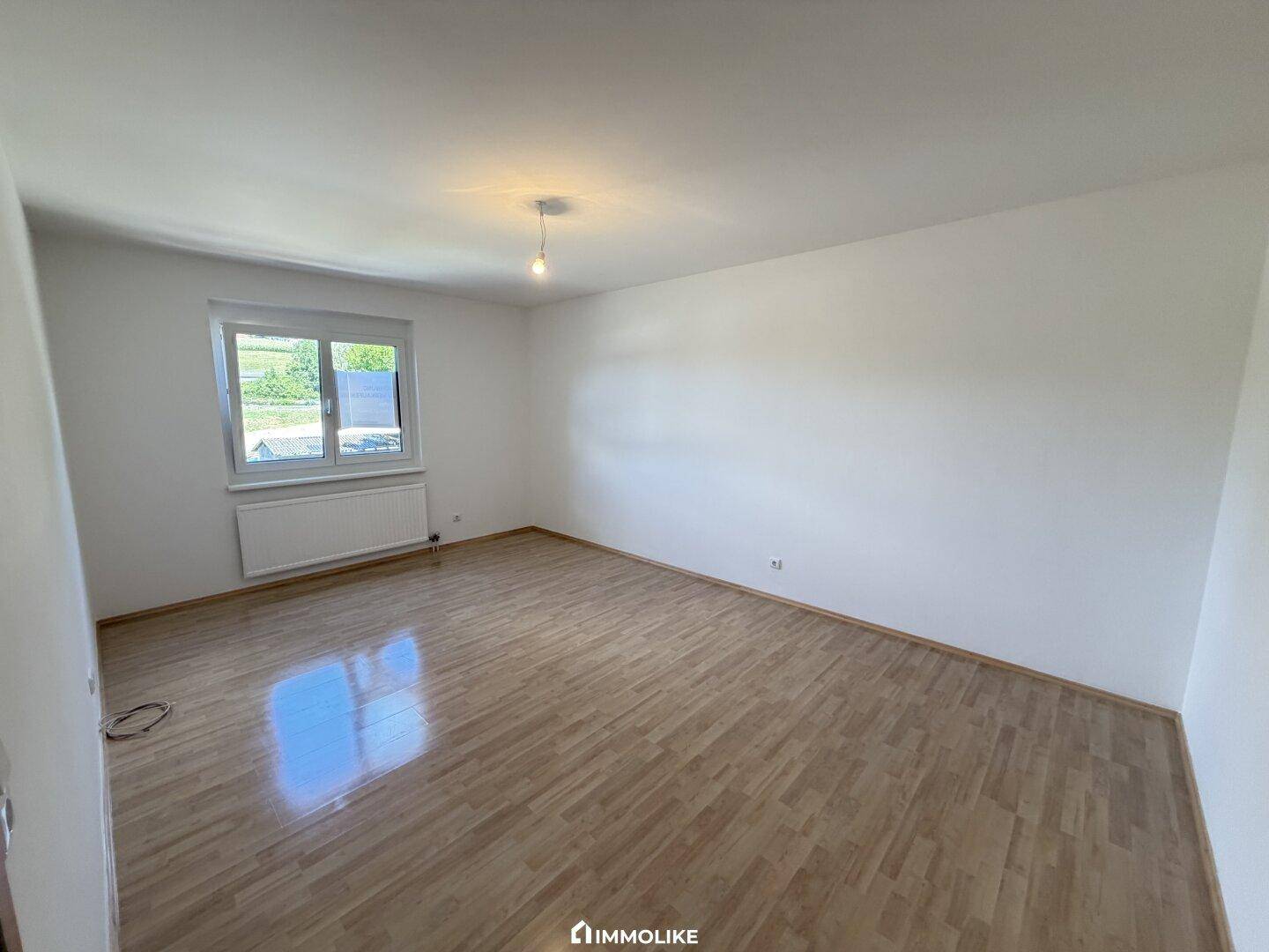 Helles Schlafzimmer mit Parkettboden und einem Fenster, das viel natürliches Licht hereinlässt.