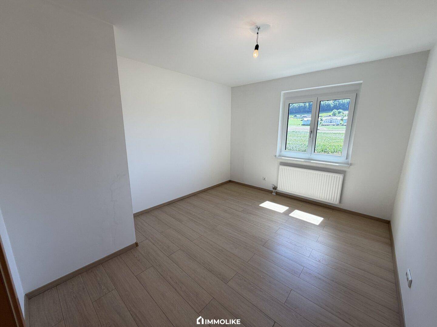 Gemütliches Schlafzimmer mit hellem Holzboden und einem Fenster mit Blick ins Grüne.