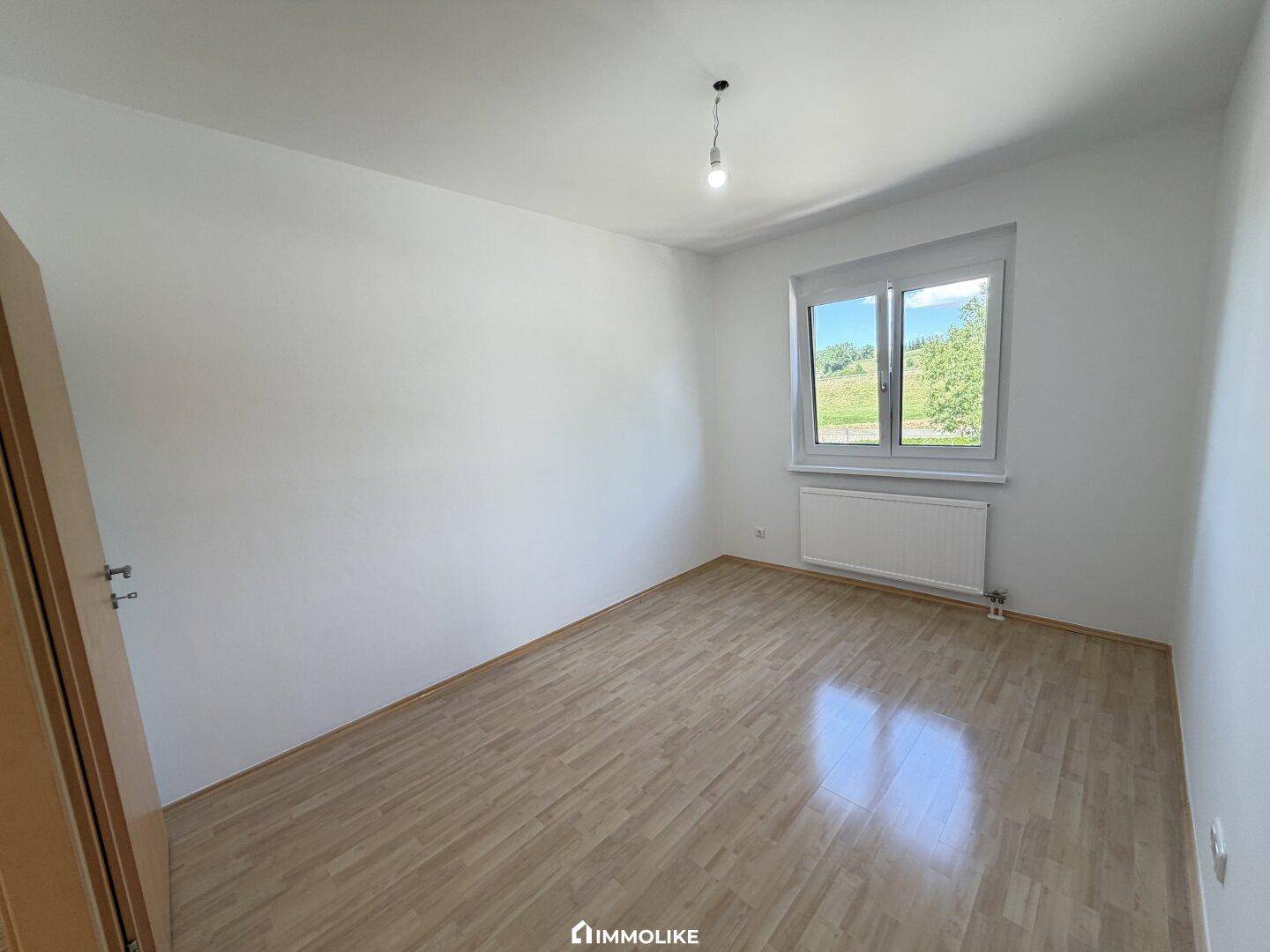 Ruhiges Schlafzimmer mit glänzendem Parkettboden und einem Fenster für angenehmes Tageslicht.