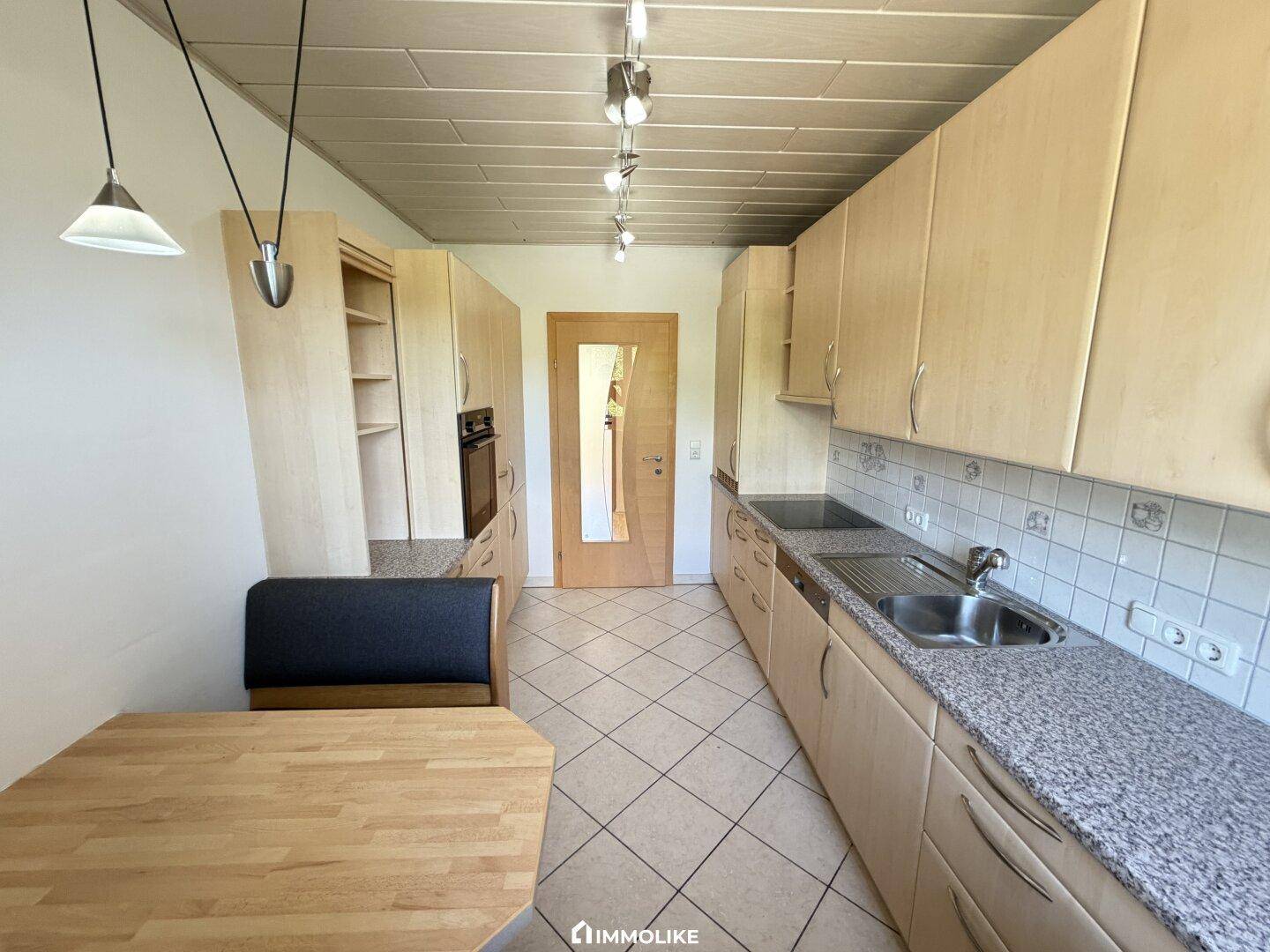 Funktionale Küche mit hellen Holzschränken, Granit-Arbeitsplatten und integriertem Essbereich.