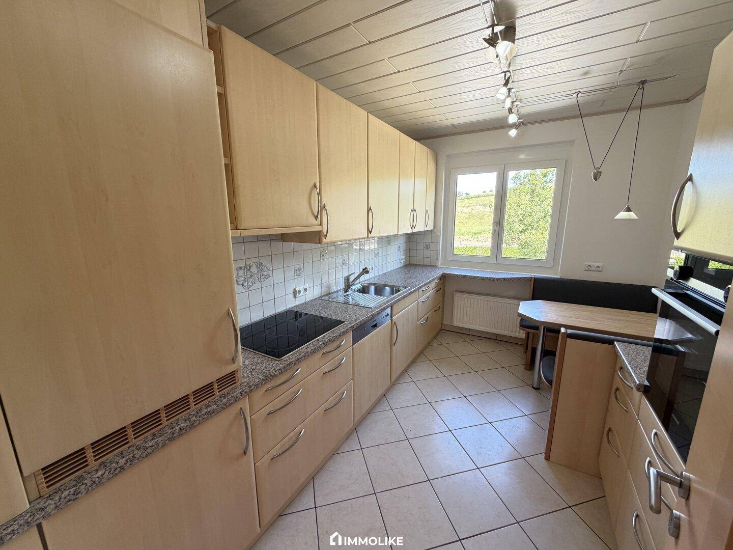 Helle Einbauküche mit Holzfronten, Fenster und einem gemütlichen Essbereich für die Familie.