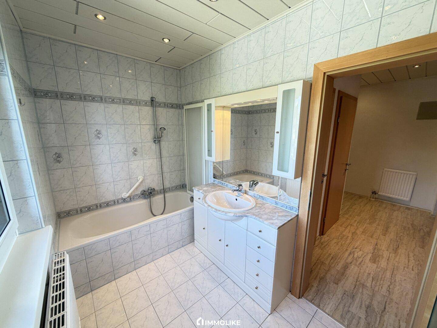 Gefliestes Badezimmer mit Badewanne, integrierter Dusche, Einzelwaschbecken und Spiegelschrank.