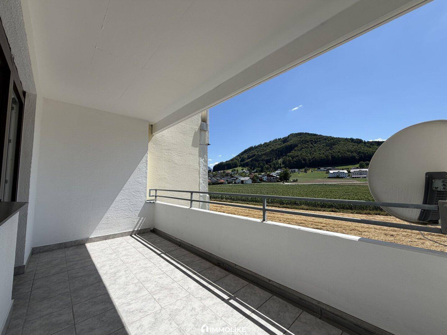 Sonniger Balkon mit Fliesenboden und weitem Blick über die umliegende Landschaft und Berge.