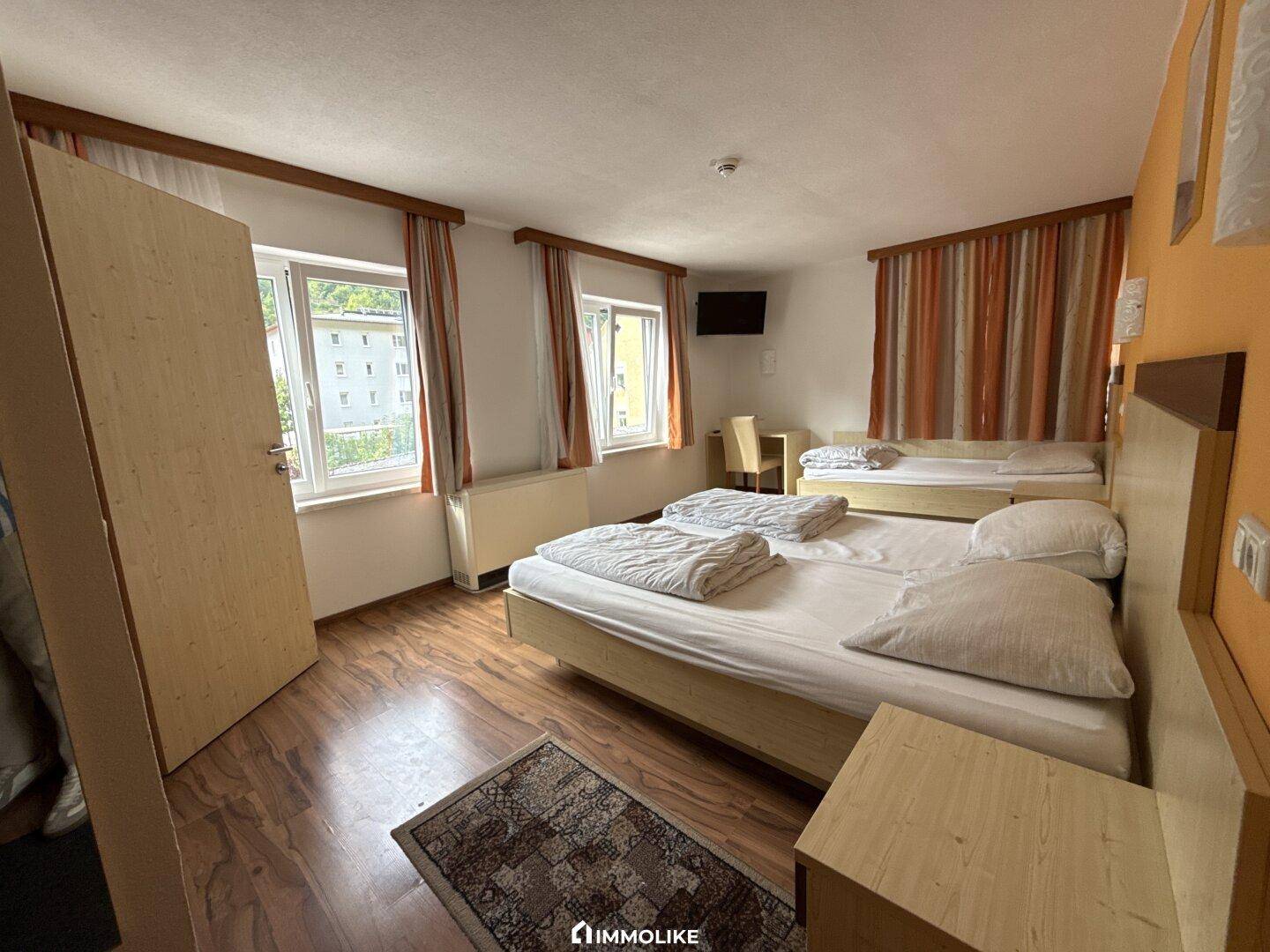 Helles Schlafzimmer mit Holzfußboden, mehreren Betten und einem Ausblick ins Grüne.