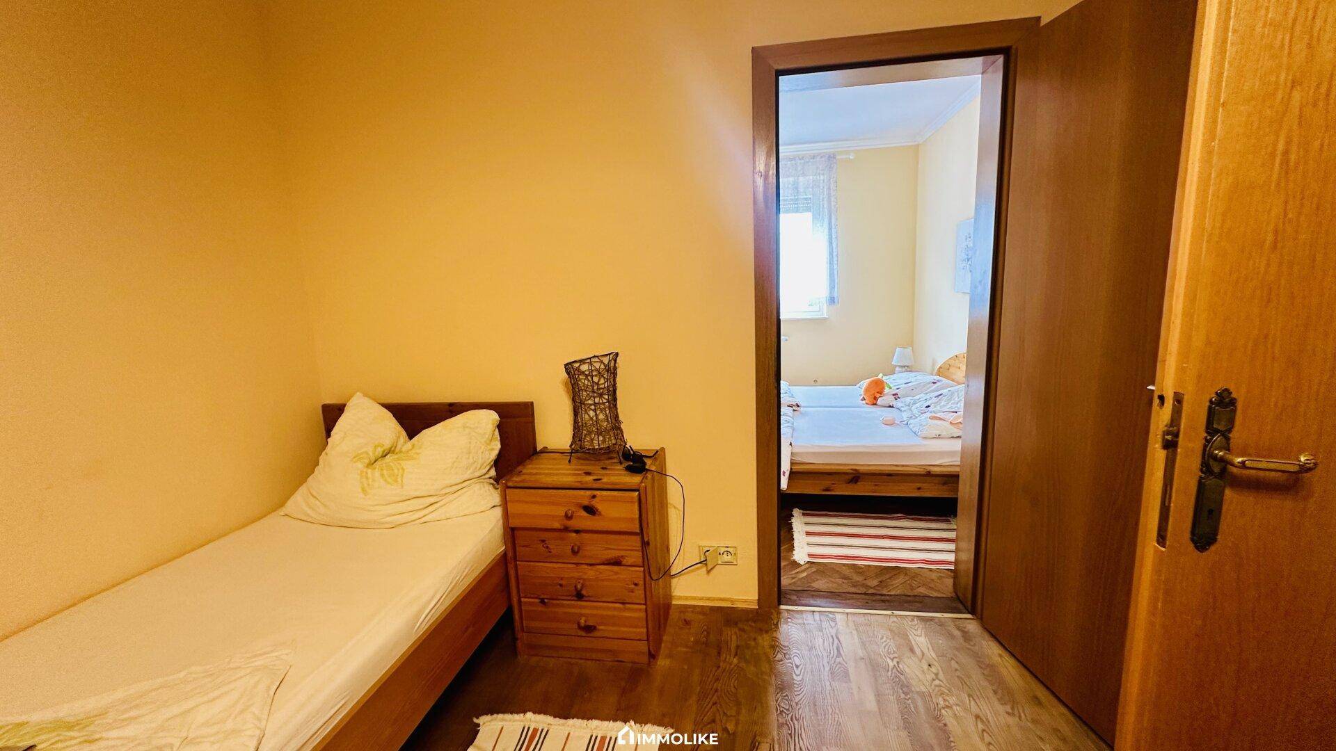 Schlafzimmer mit Einzelbett und Blick durch die Tür in ein weiteres Zimmer.