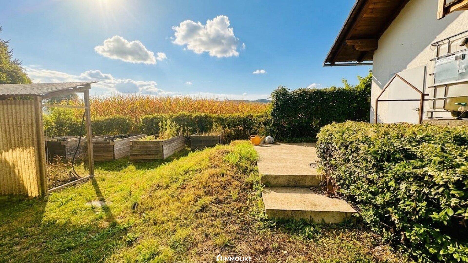 Gartenbereich mit Hochbeeten und weitem Blick auf die umliegenden Felder.