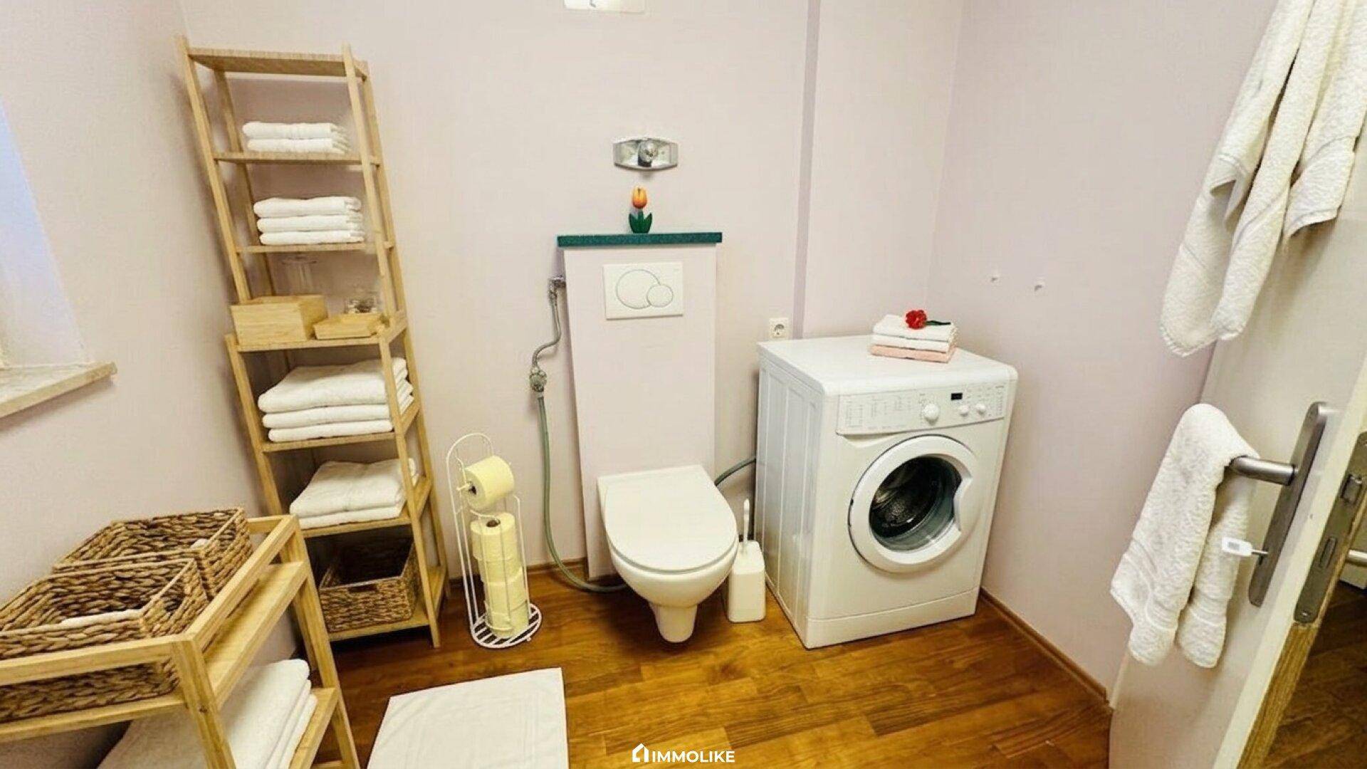 Separates WC mit Waschmaschine, Holzregal und Fenster.