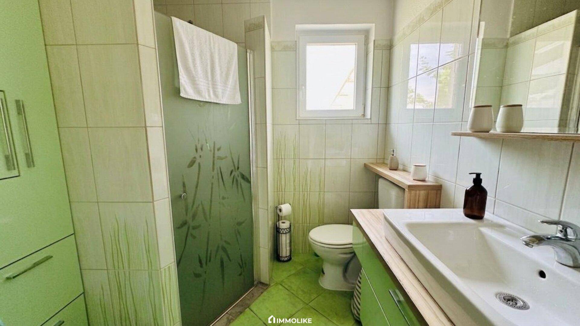 Modernes Badezimmer in Grün mit Dusche, Waschbecken und Fenster.