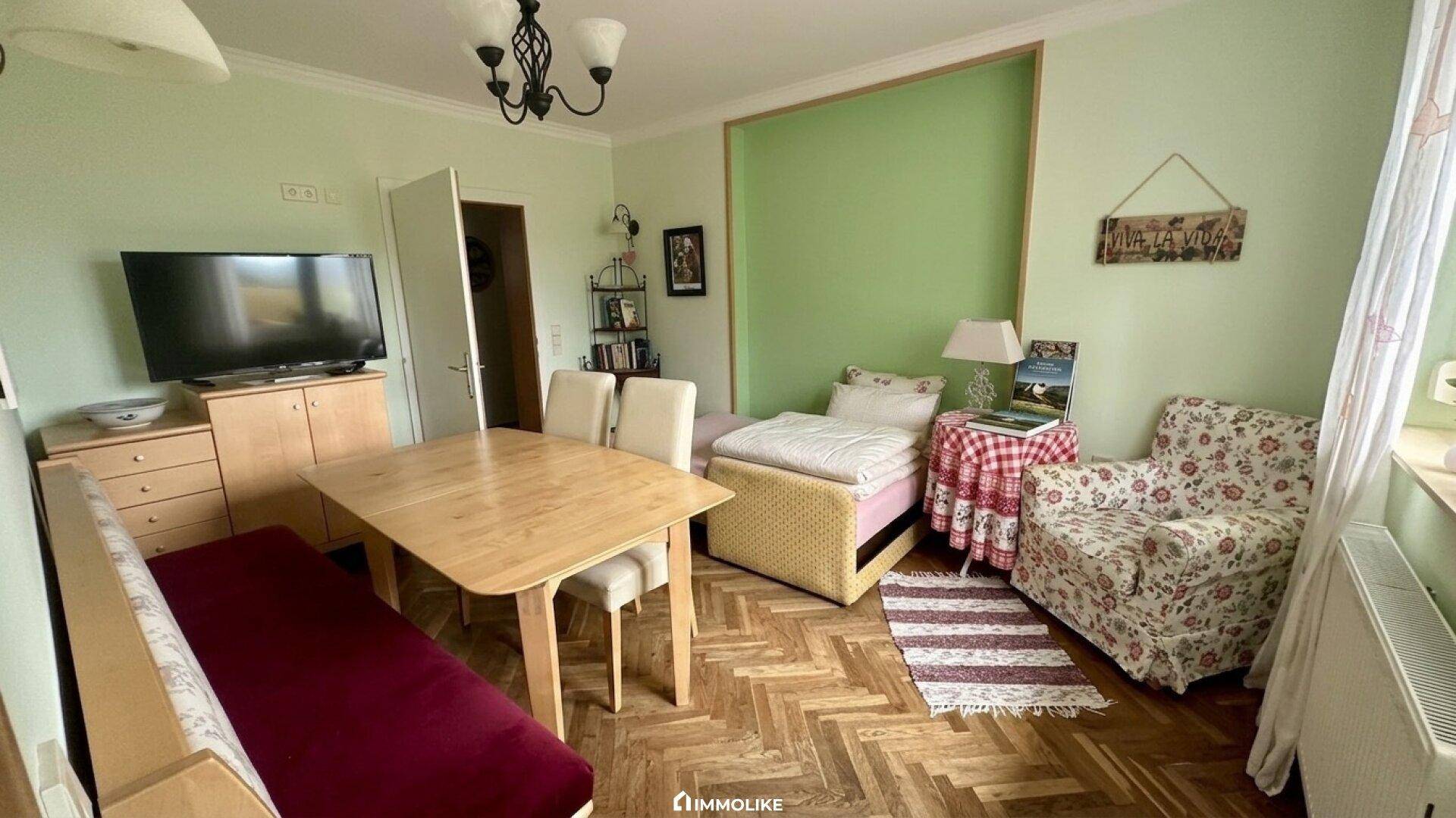 Helles Schlafzimmer mit Parkettboden, Esstisch und grün gestrichenen Wänden.