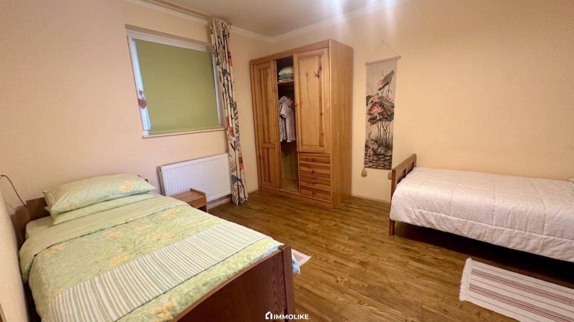 Schlafzimmer mit zwei Einzelbetten, Holzschrank und Fenster.