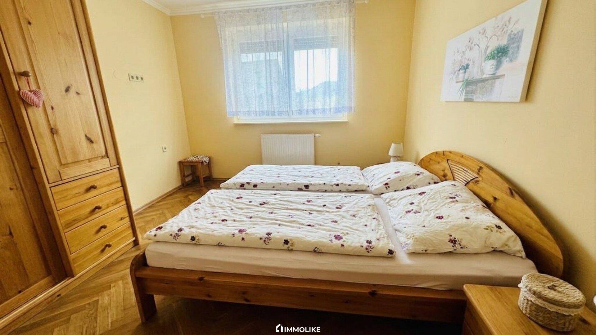 Helles Schlafzimmer mit Doppelbett, Holzschrank und Fenster.