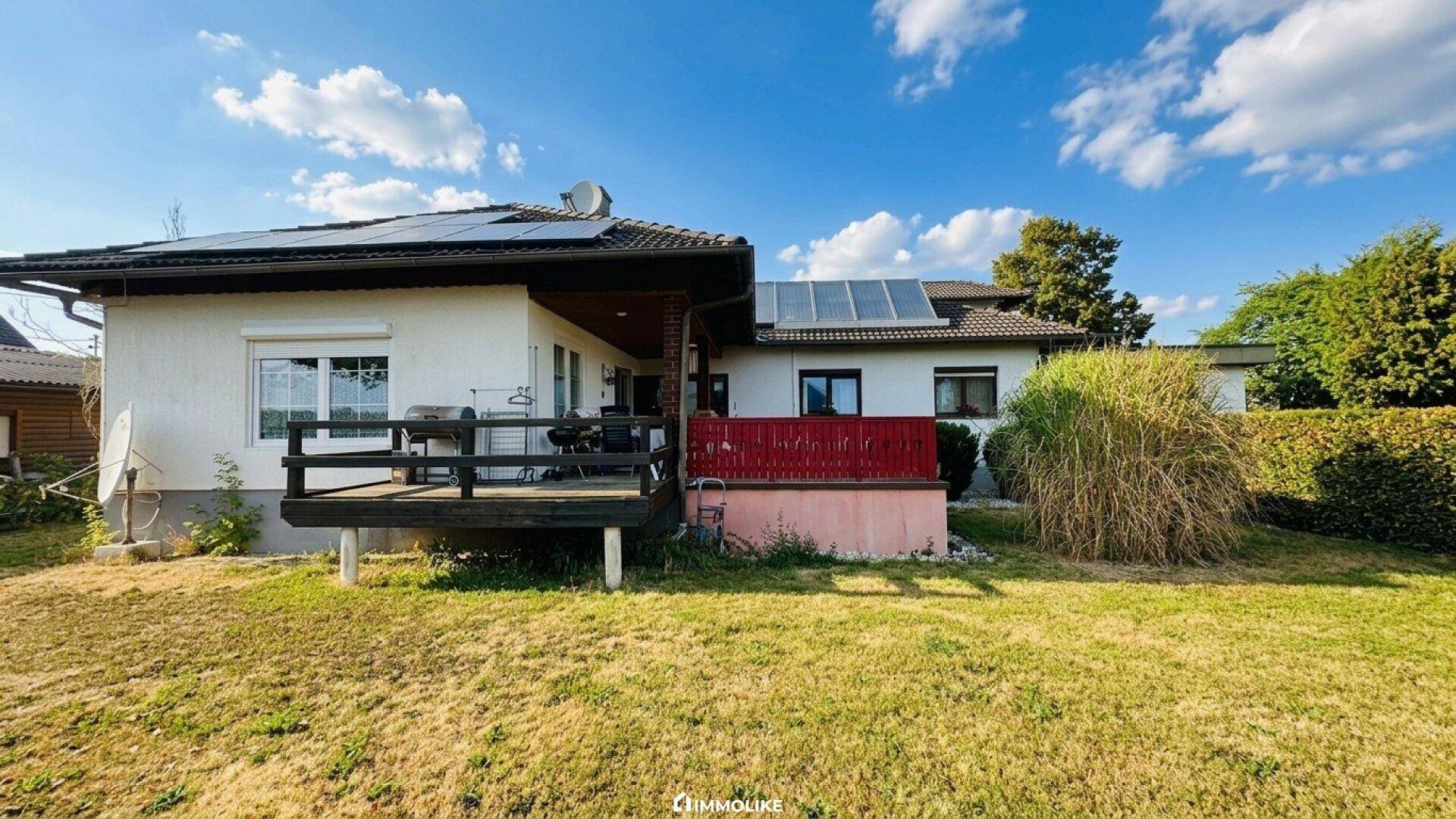 Hinterer Gartenbereich mit Rasenfläche, Terrasse und Solaranlage auf dem Dach.