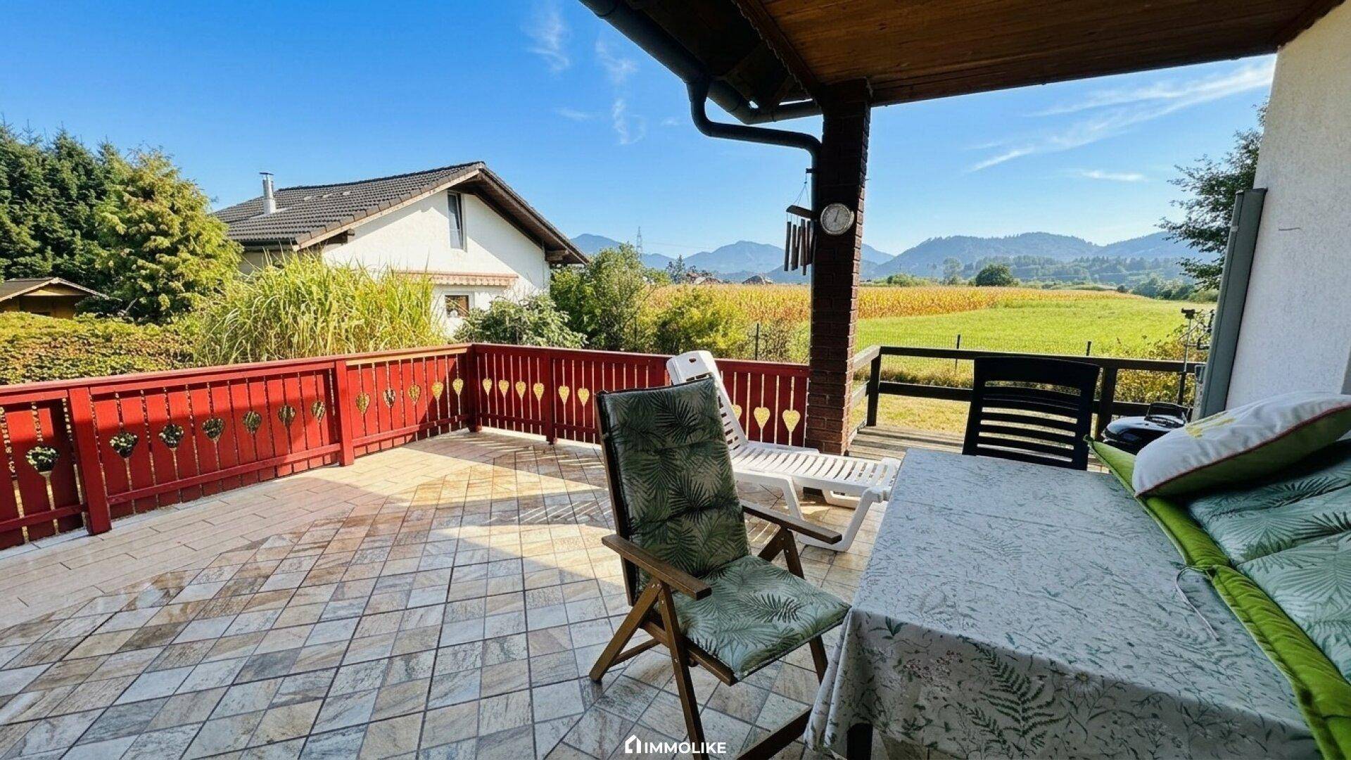 Geräumige Terrasse mit Fliesenboden, rotem Geländer und weitem Blick über Felder und Berge.